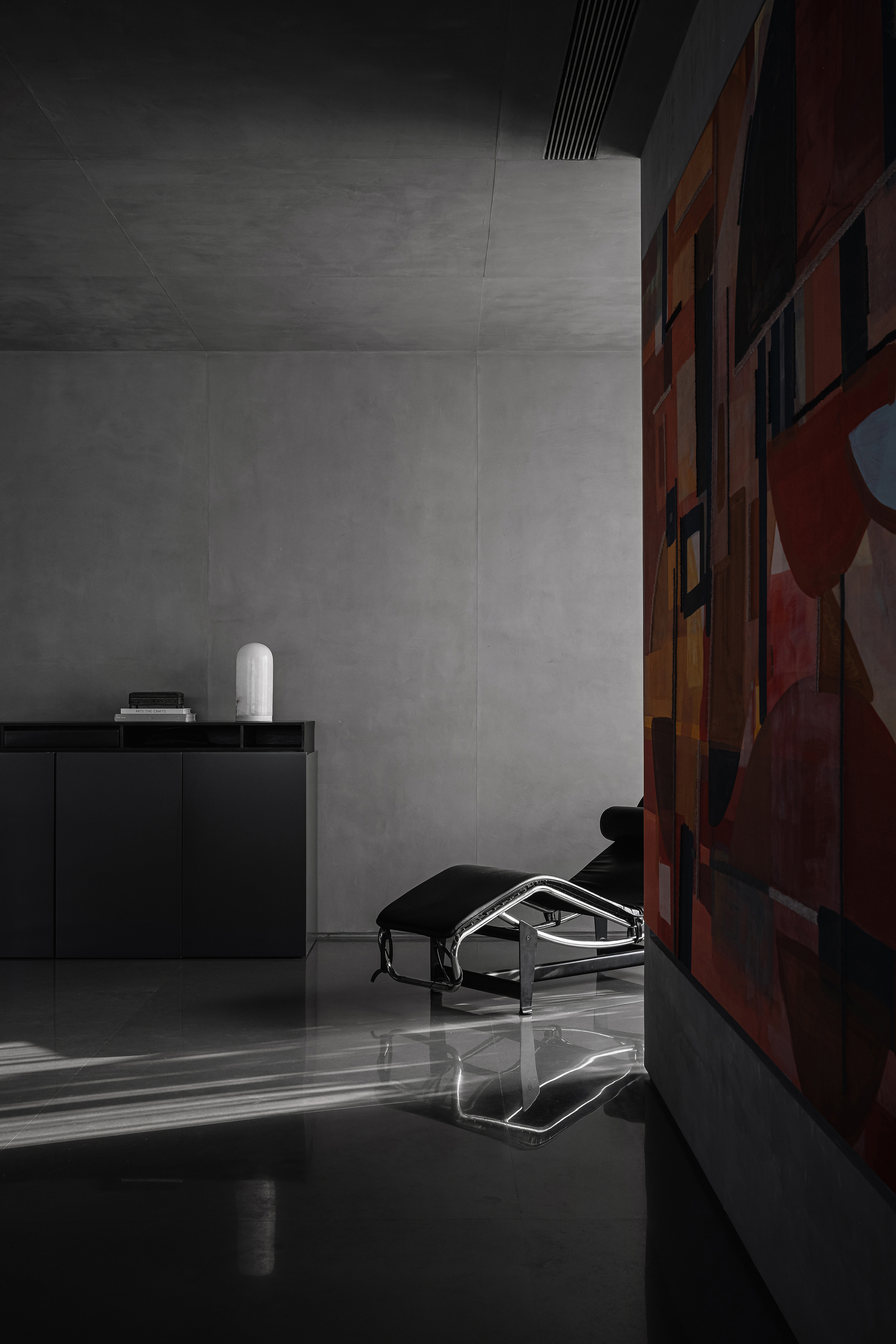 Interior corner with grey concrete walls and a low armchair beside a colorful abstract painting