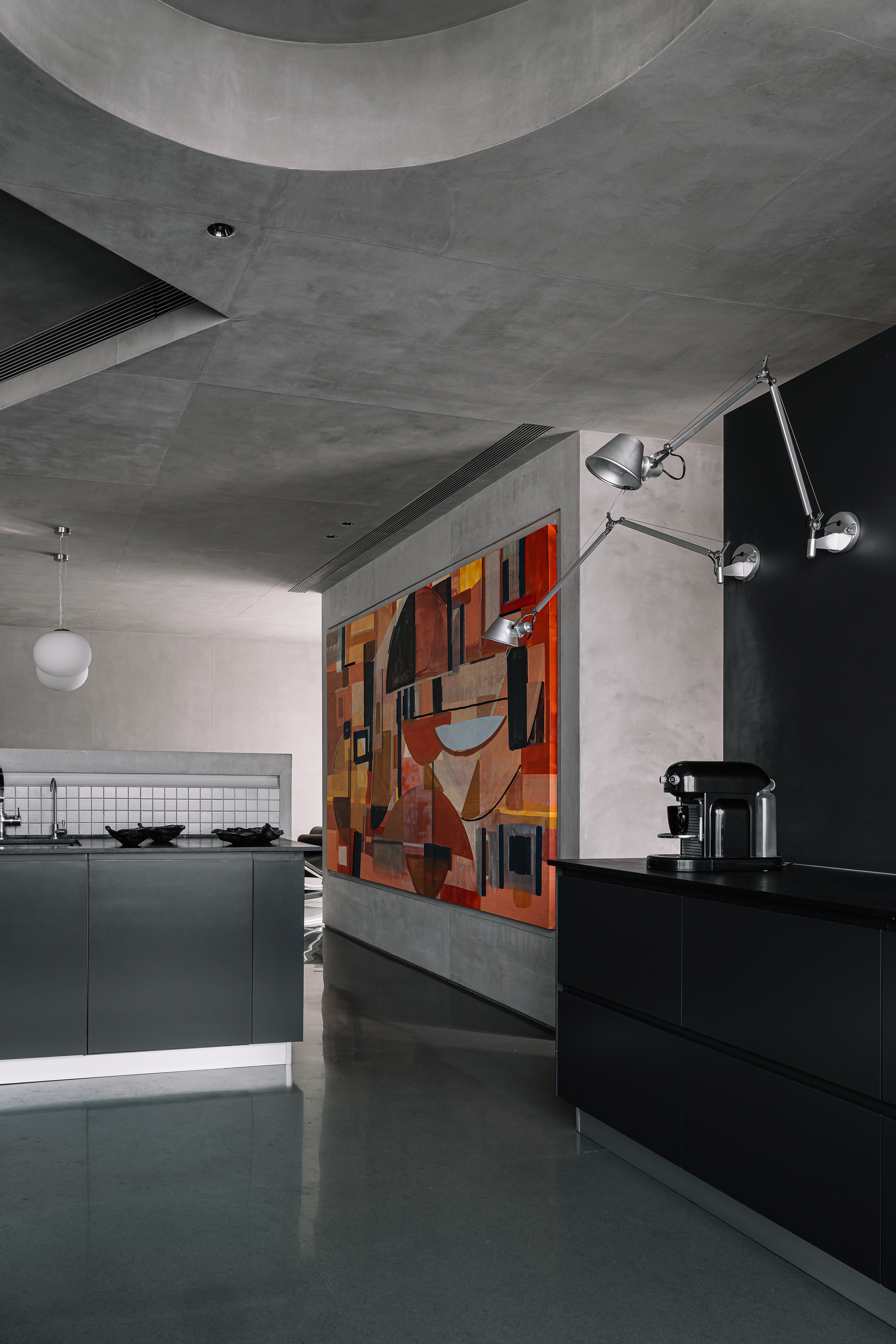 Kitchen area with black cabinetry and colorful geometric mural behind a grey concrete partition wall