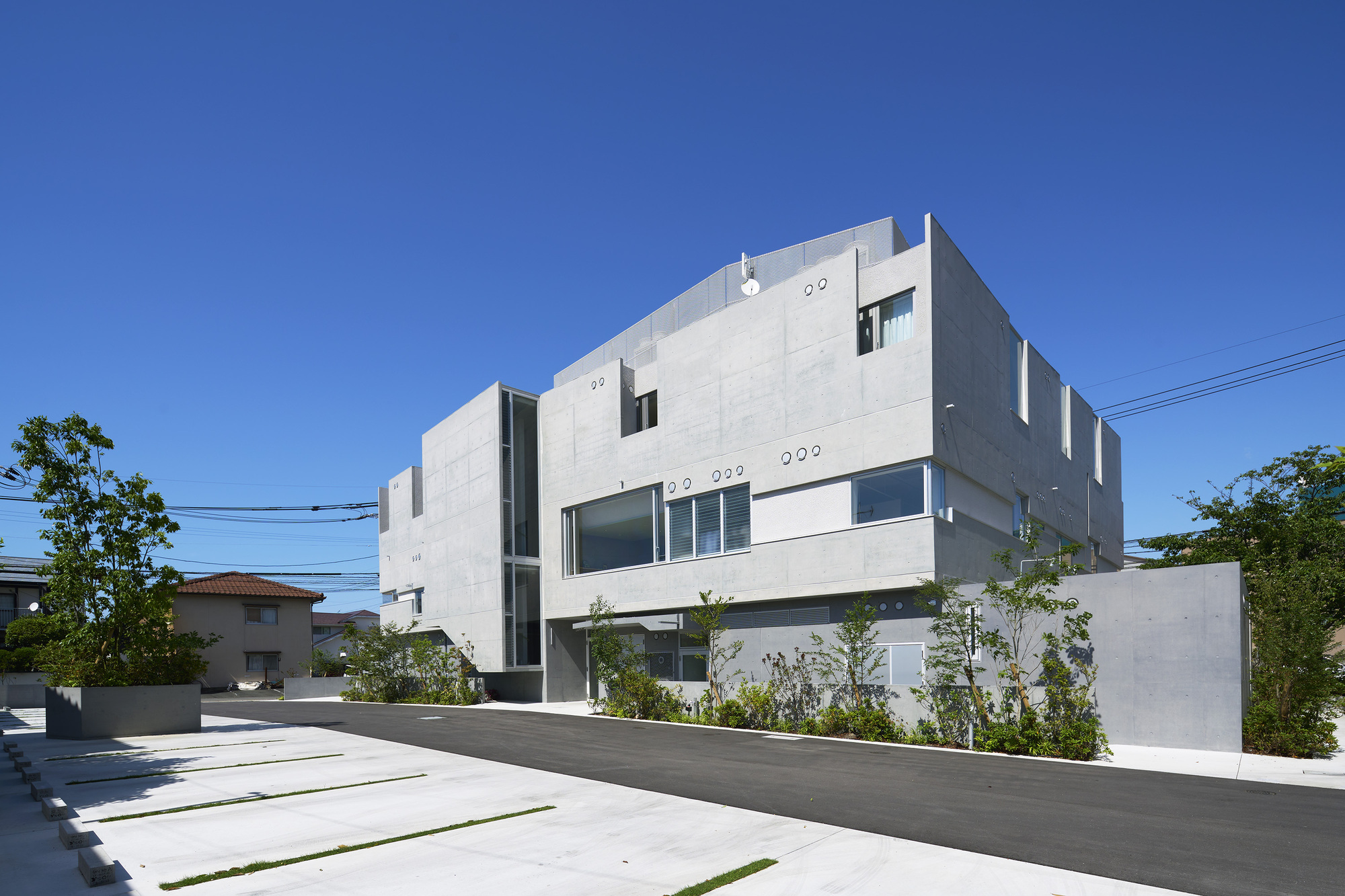 Street view of the white concrete volumes with varied window openings under a clear blue sky