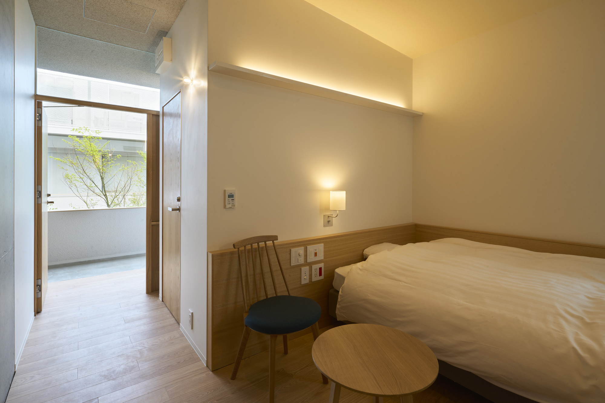 Bedroom with timber headboard and open door leading to a small terrace with tree