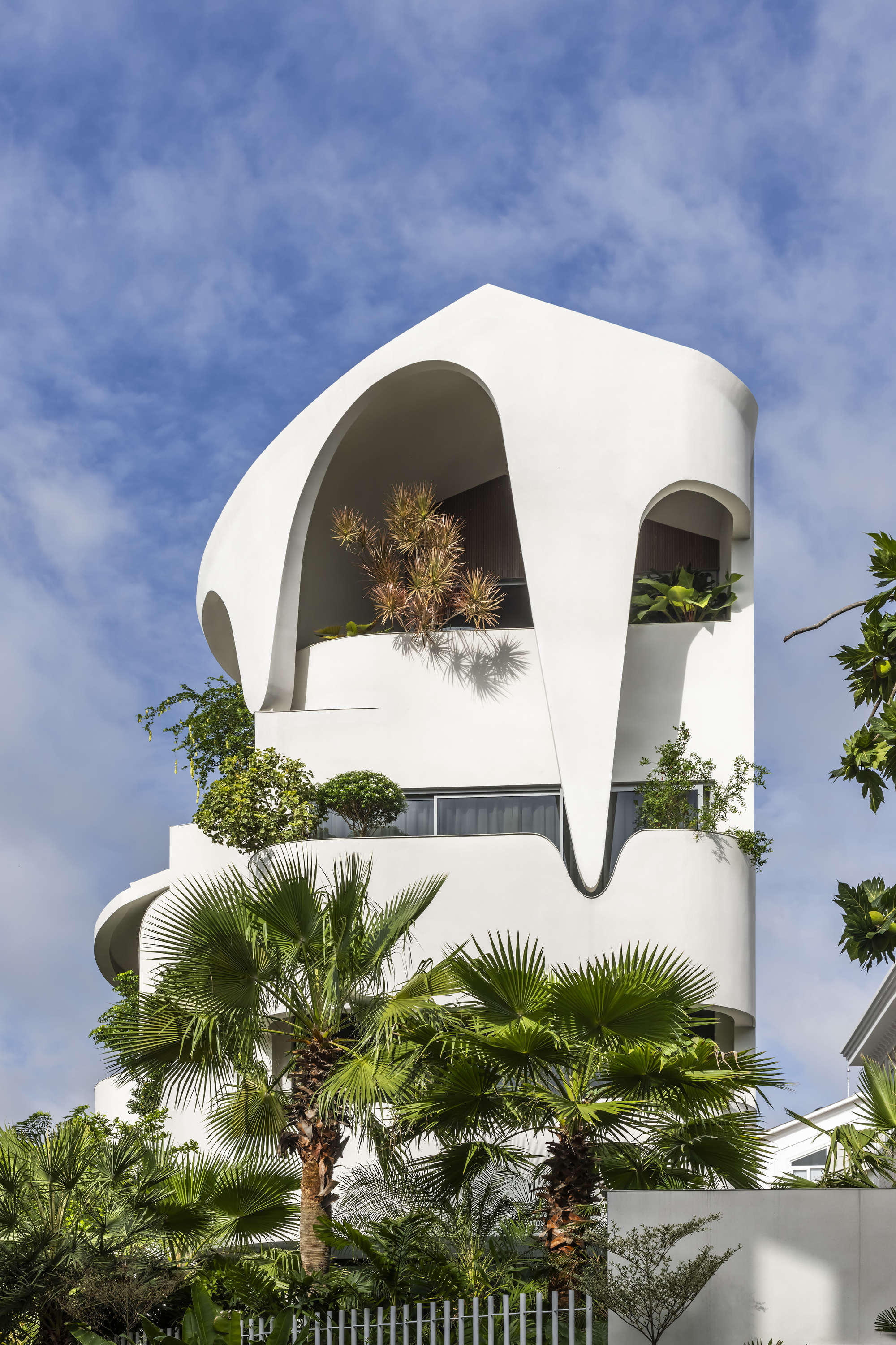 White facade with large arched openings framing potted pines against a clear blue sky