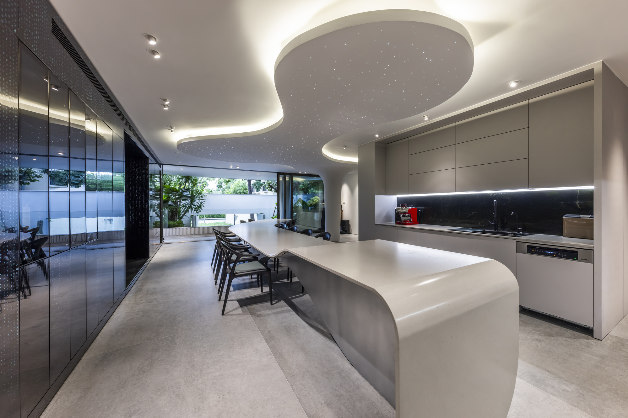 Kitchen and dining space with curved island beneath an organic ceiling cutout overlooking the courtyard