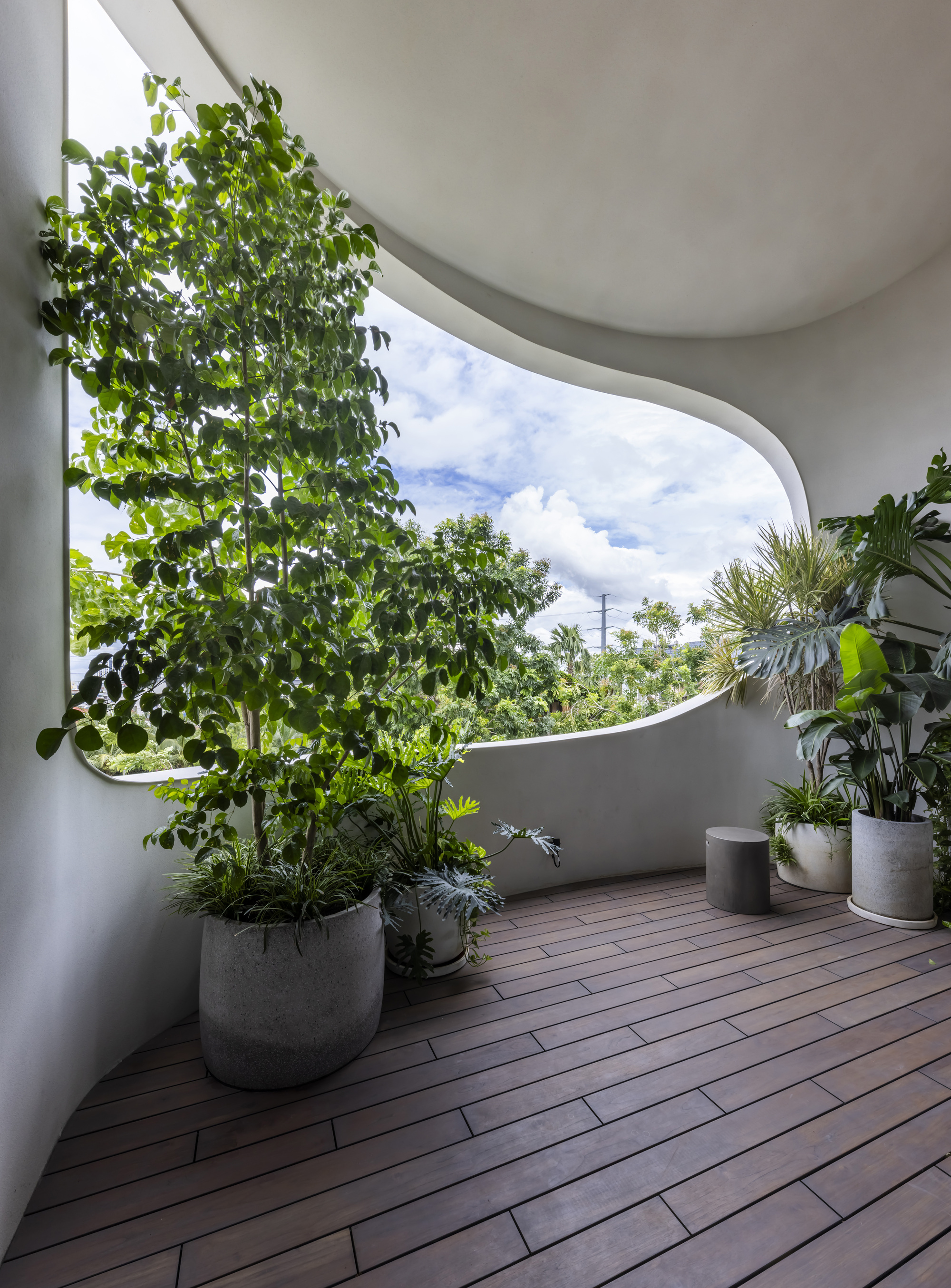 Curved balcony with timber decking and concrete planters under a partly cloudy sky