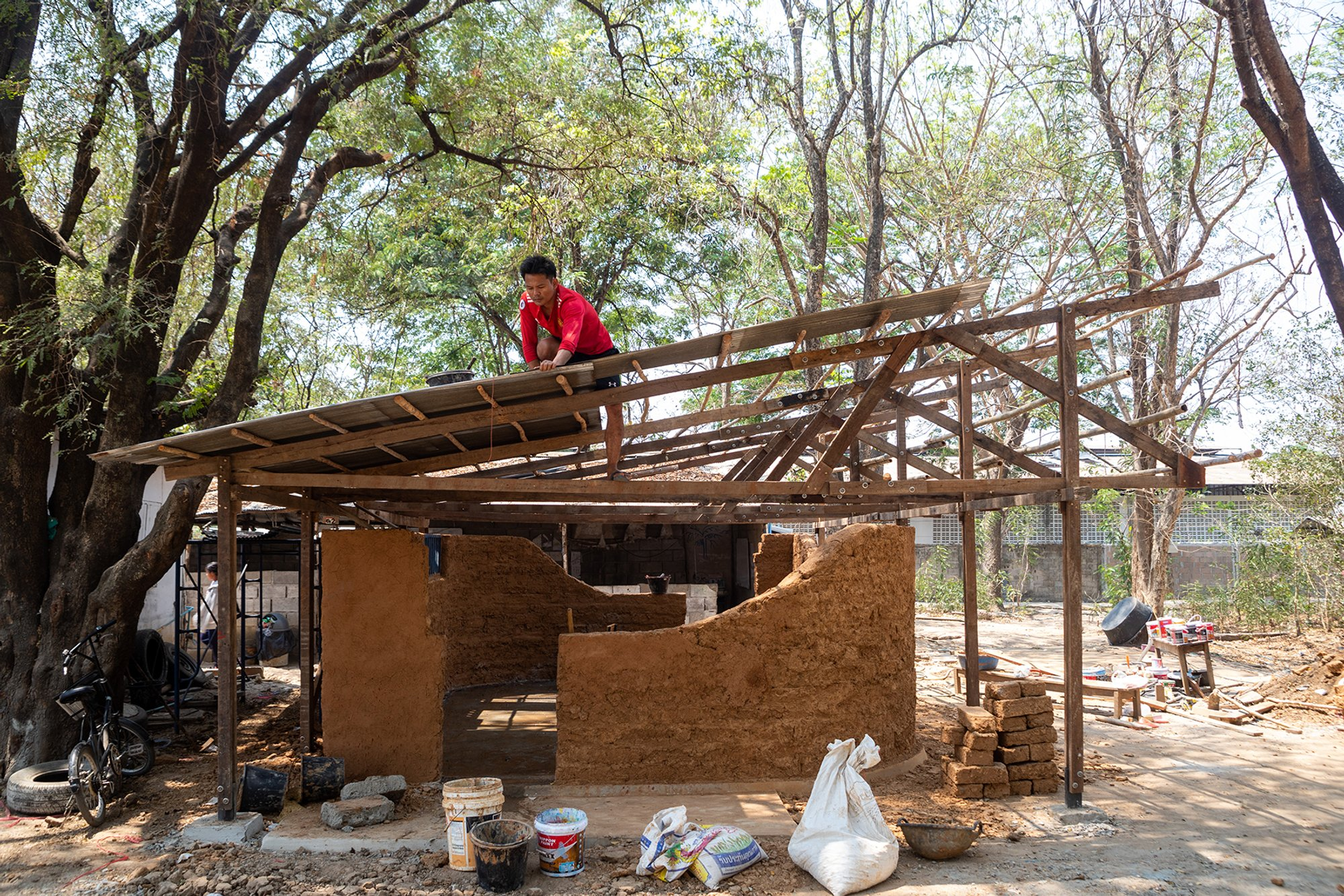  Timber roof structure assembled over hand-sculpted earth walls in a low-cost classroom build. 