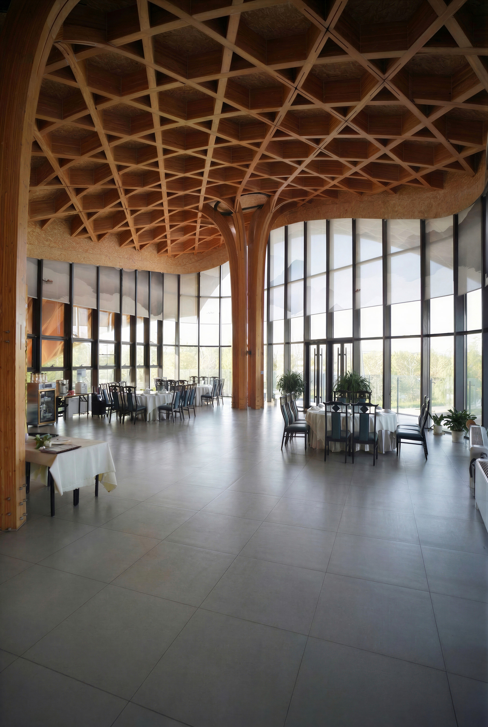 Interior dining space with timber lattice ceiling, branching wooden columns, and curtain wall overlooking landscape