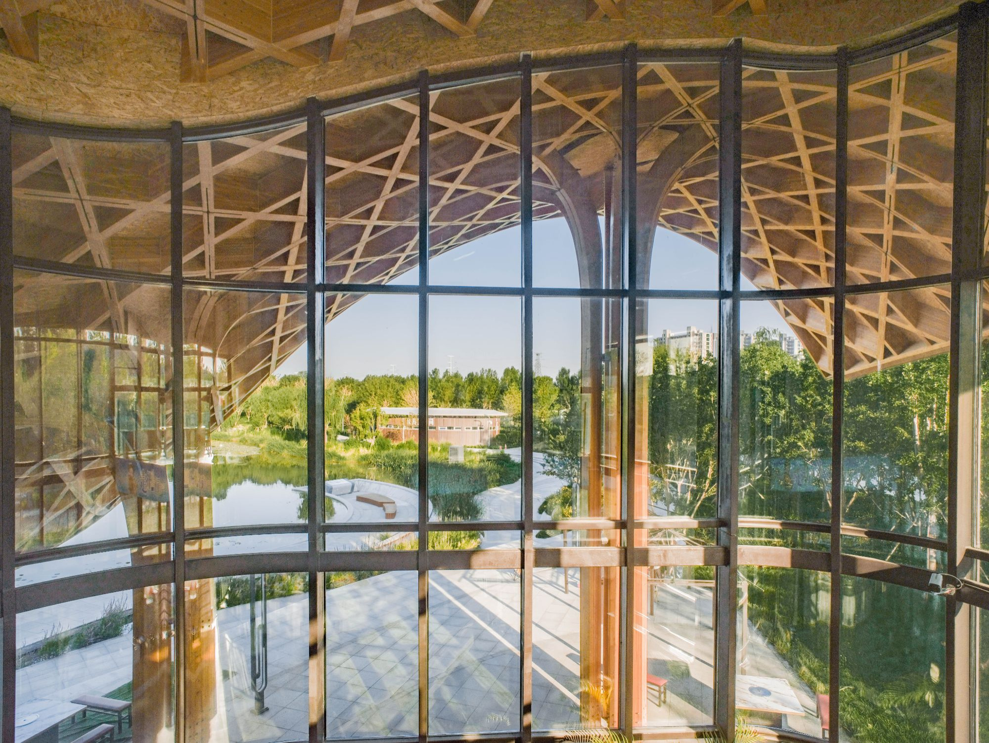 Floor-to-ceiling steel-framed glazing reflecting the timber lattice structure and overlooking the water and terrace