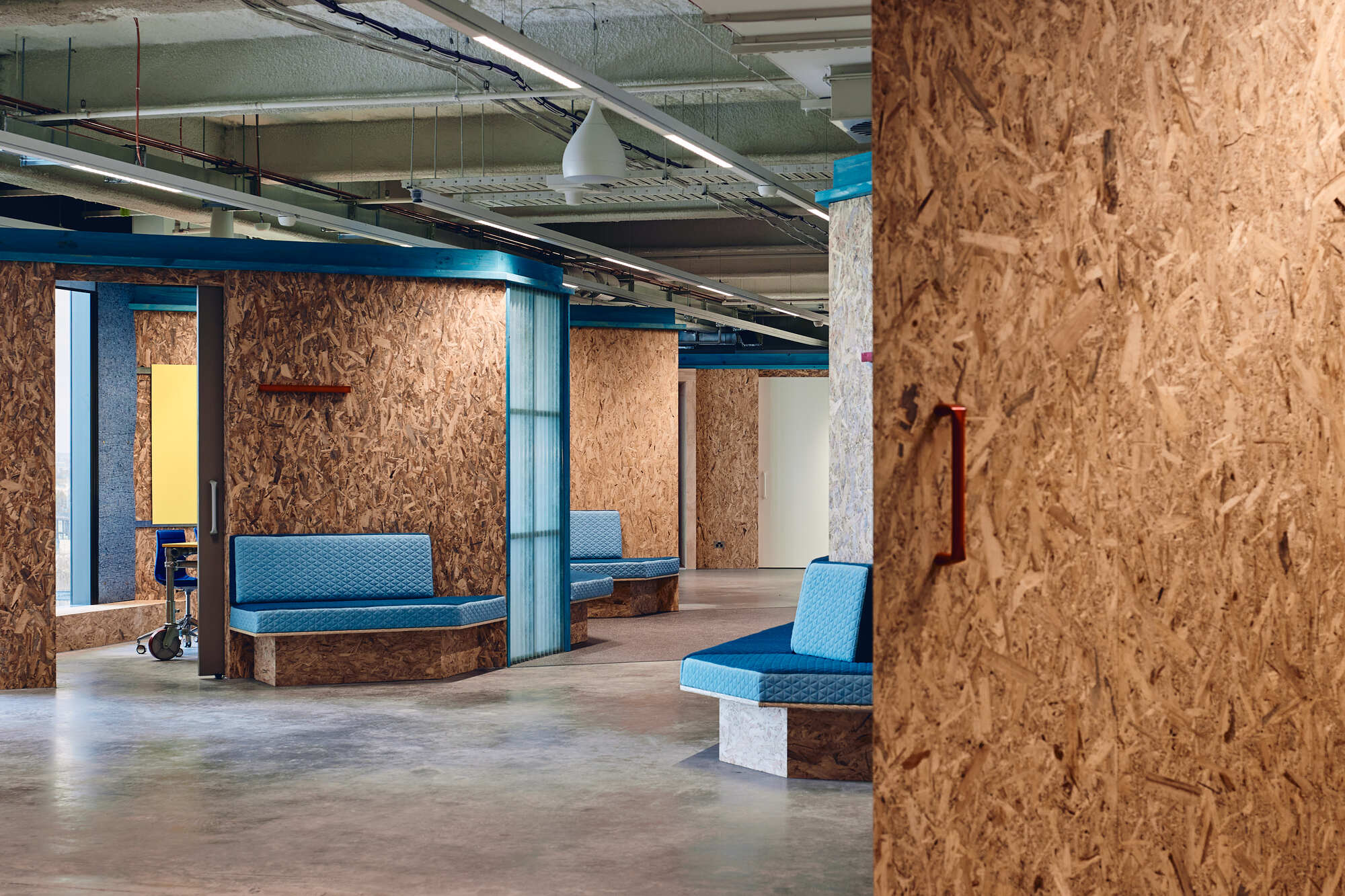 Seating clusters with turquoise cushions on oriented strand board bases around painted concrete columns
