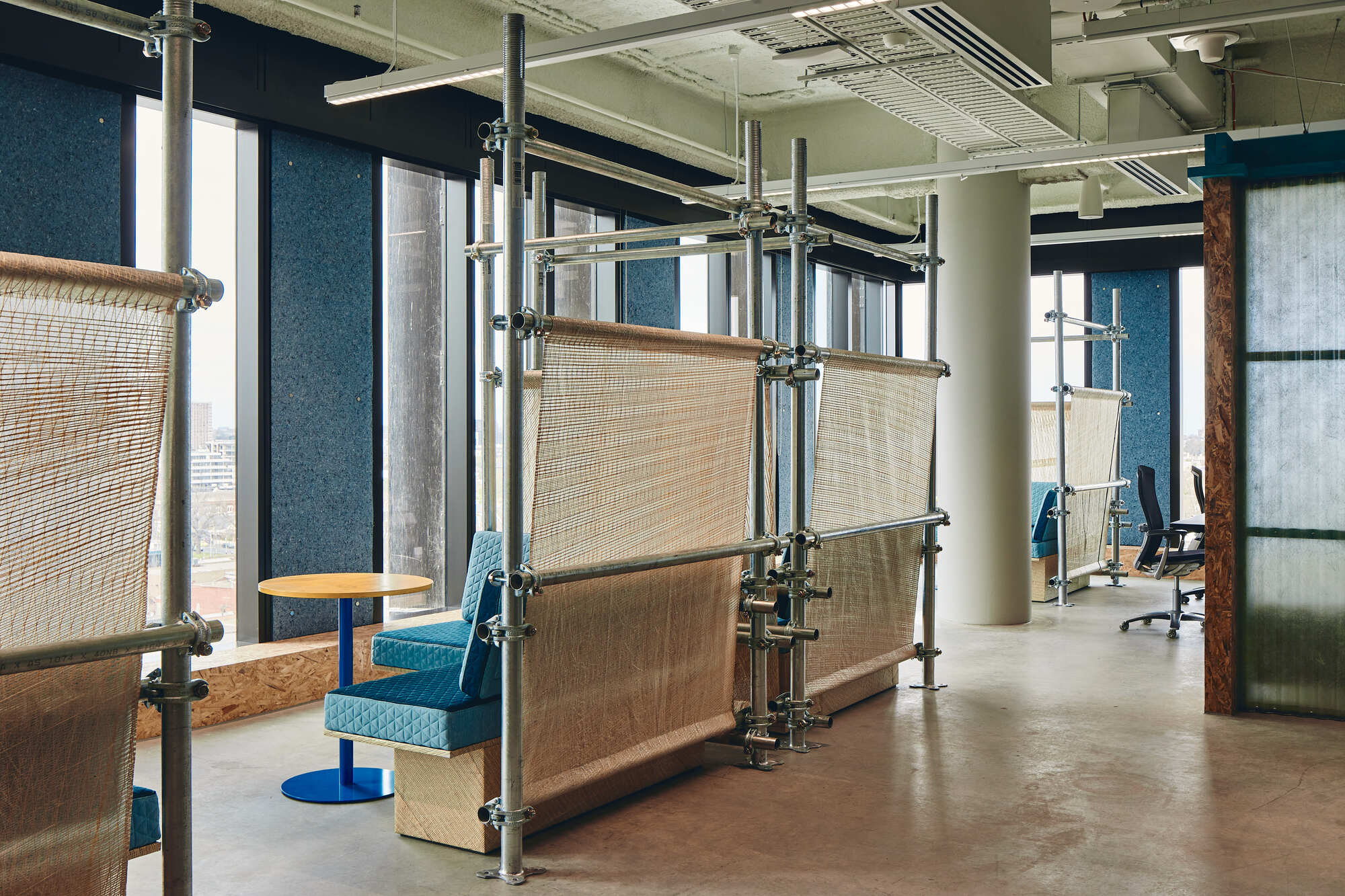Modular scaffolding partition system supporting woven textile screens beside a blue swivel chair