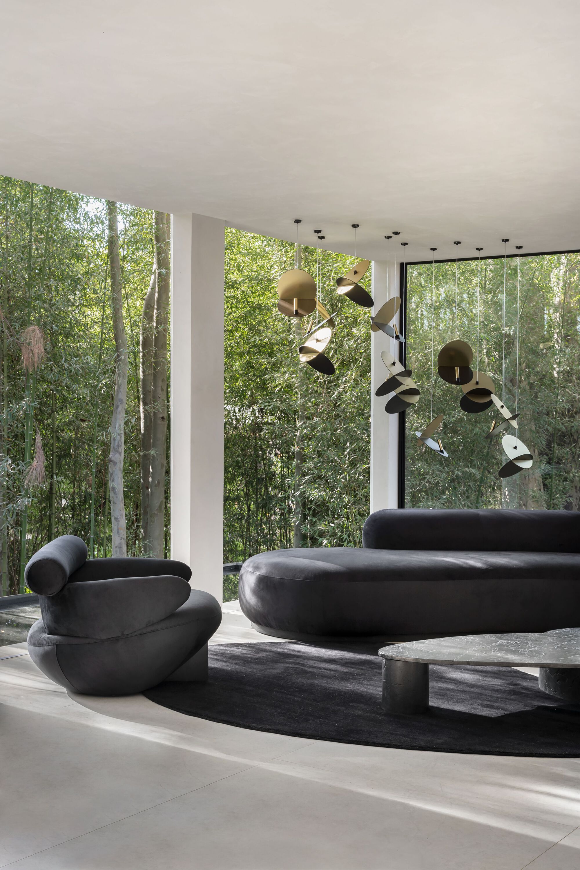 Living room with sculptural seating and pendant installation facing the glass walls and trees
