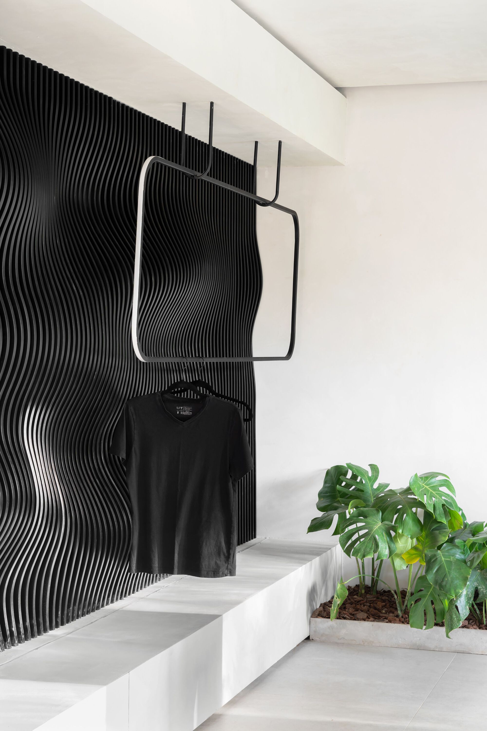Black ribbed wall panel behind a steel clothing rack and white stepped seating with potted plants