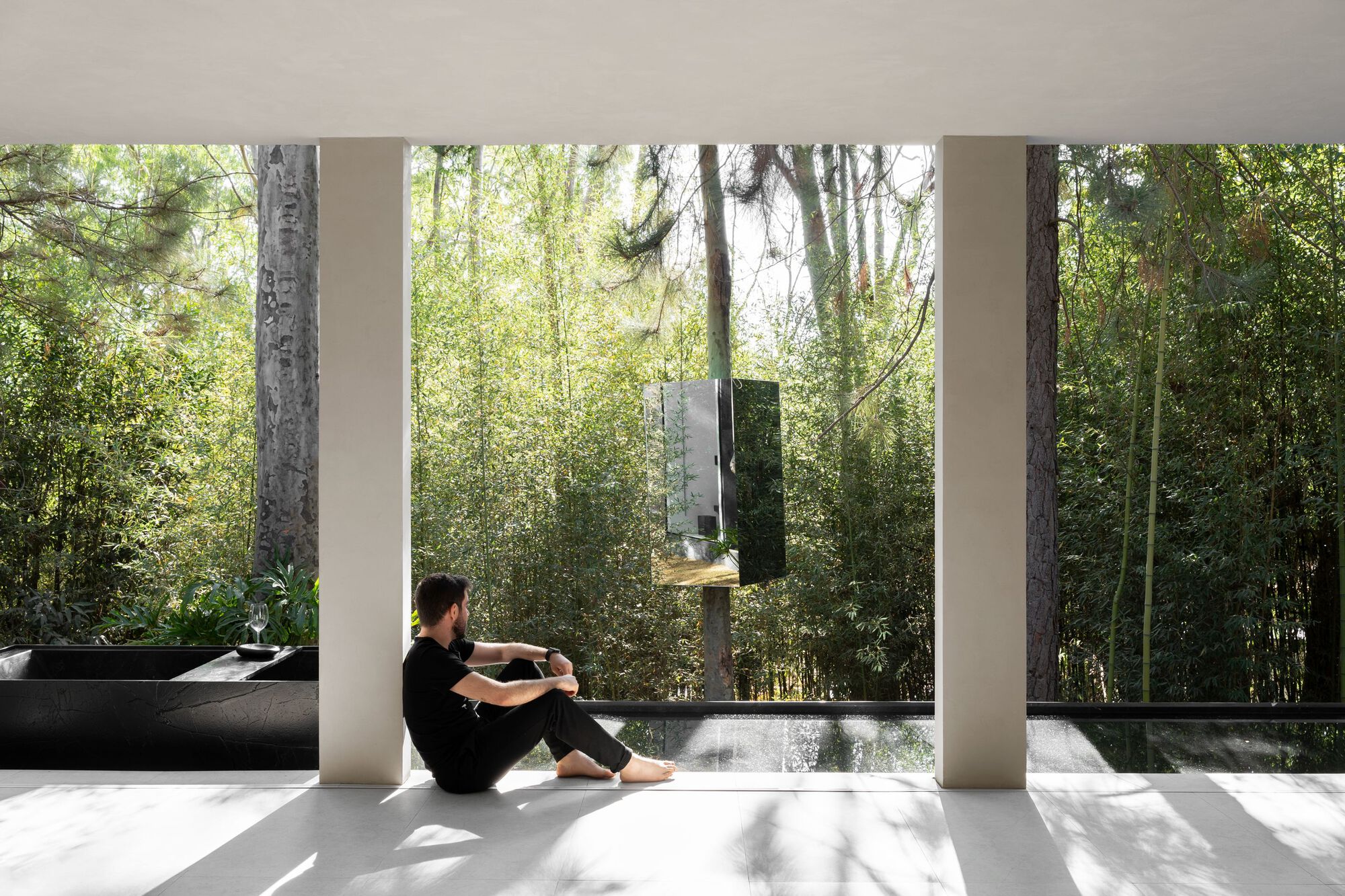 Figure seated on the floor between columns framing a view of trees and forest beyond