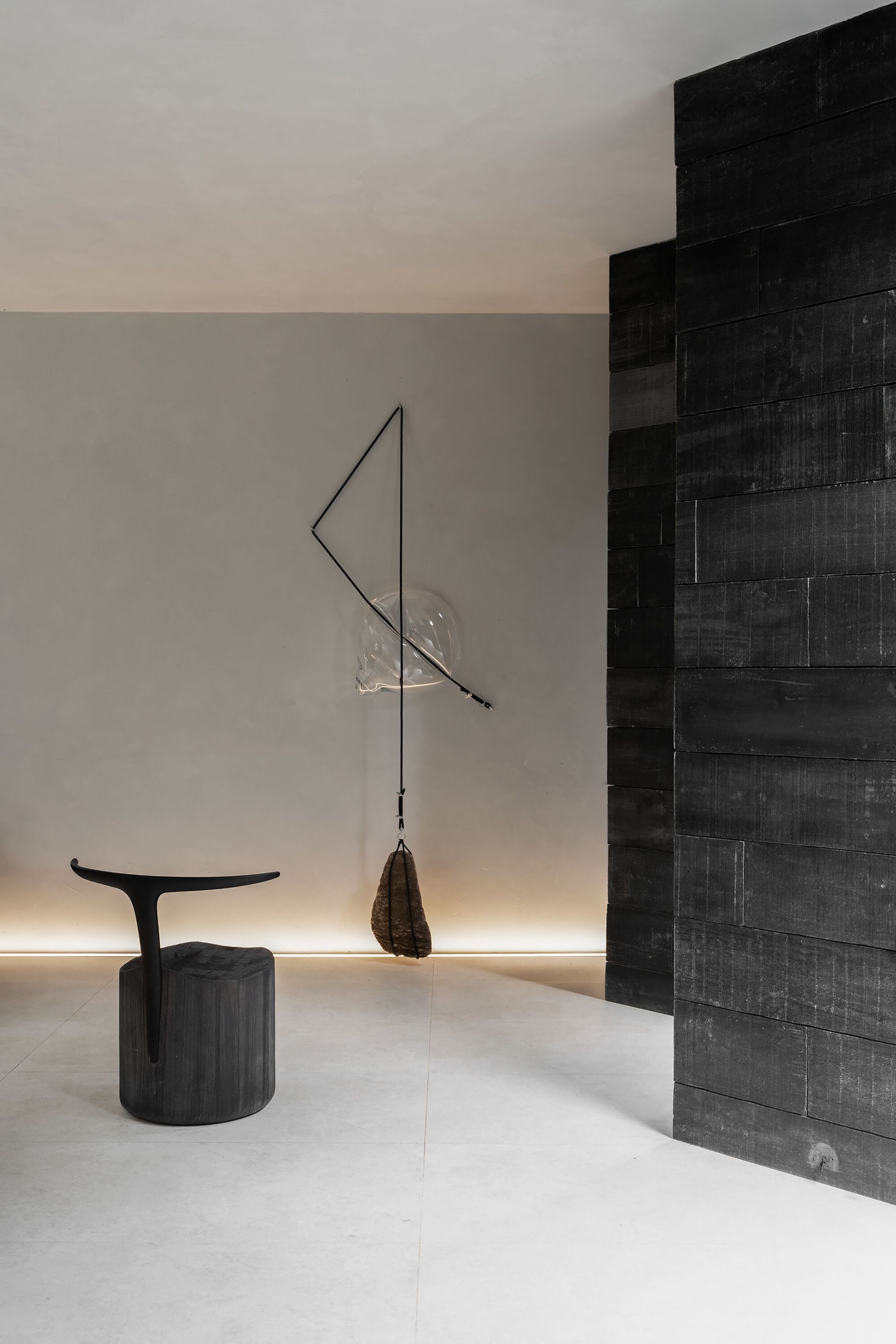 Detail of a wire sculpture and round side table beside a black tiled wall with linear uplighting