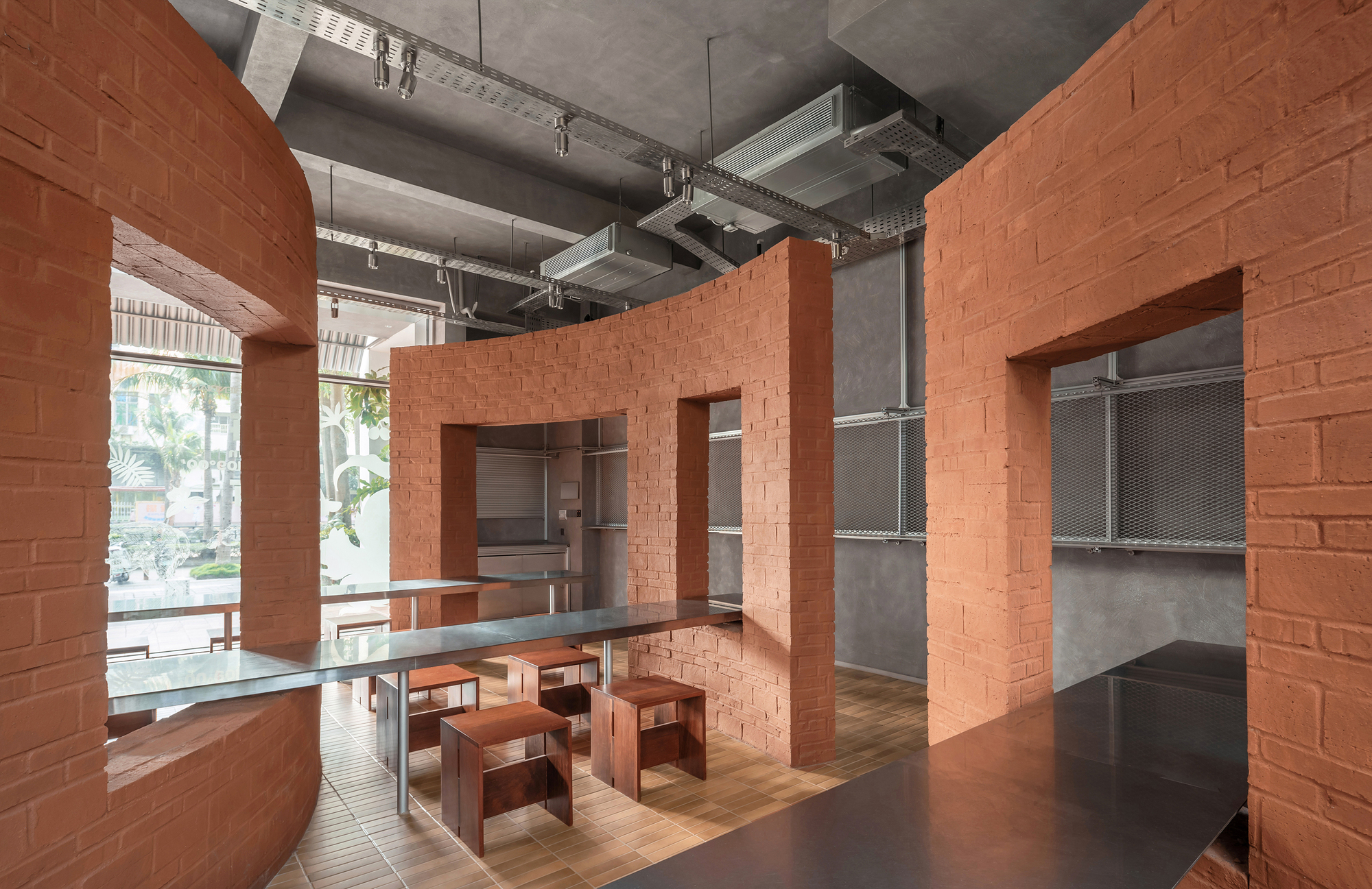 Interconnected terracotta brick volumes with large openings and shared dining table under raw concrete beams
