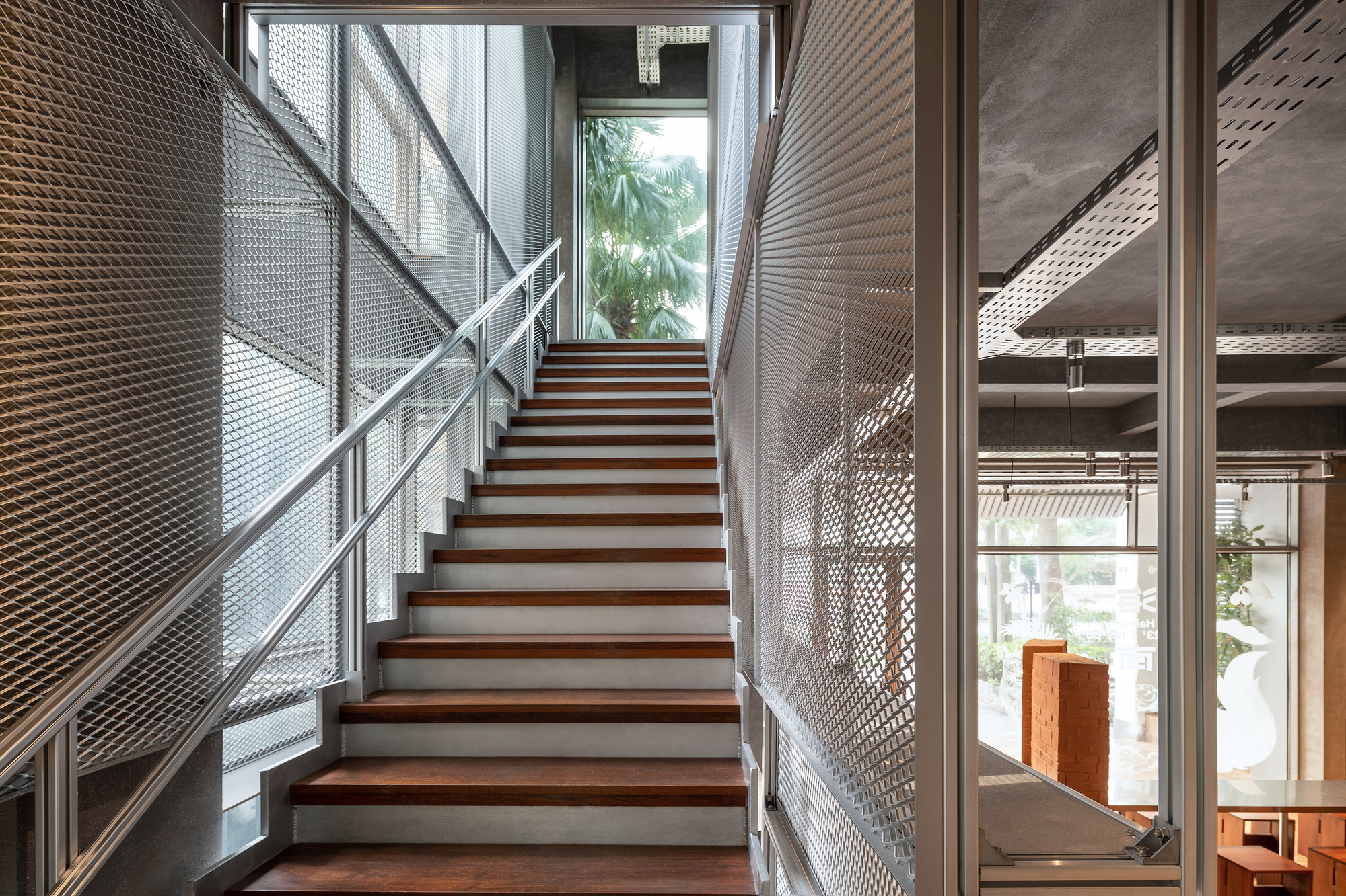 Timber-treaded staircase with expanded metal mesh railings and perforated metal walls filtering daylight