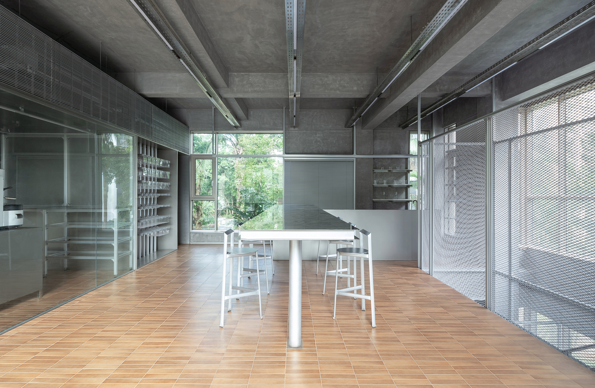 Long communal table surrounded by white stools beneath exposed concrete beams and service ducts