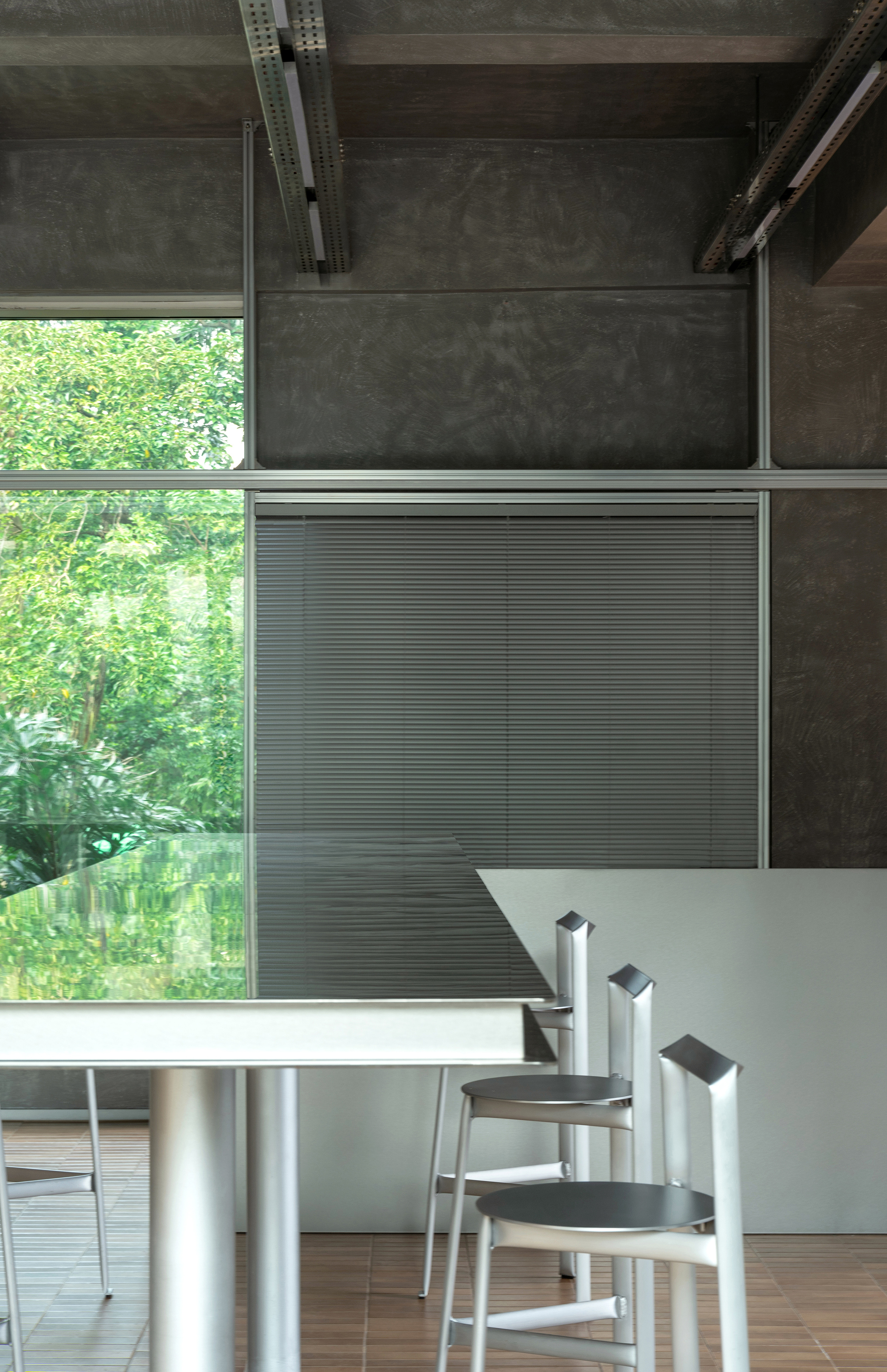 Detail of corrugated metal panel and stacked stools beside the communal table overlooking green foliage
