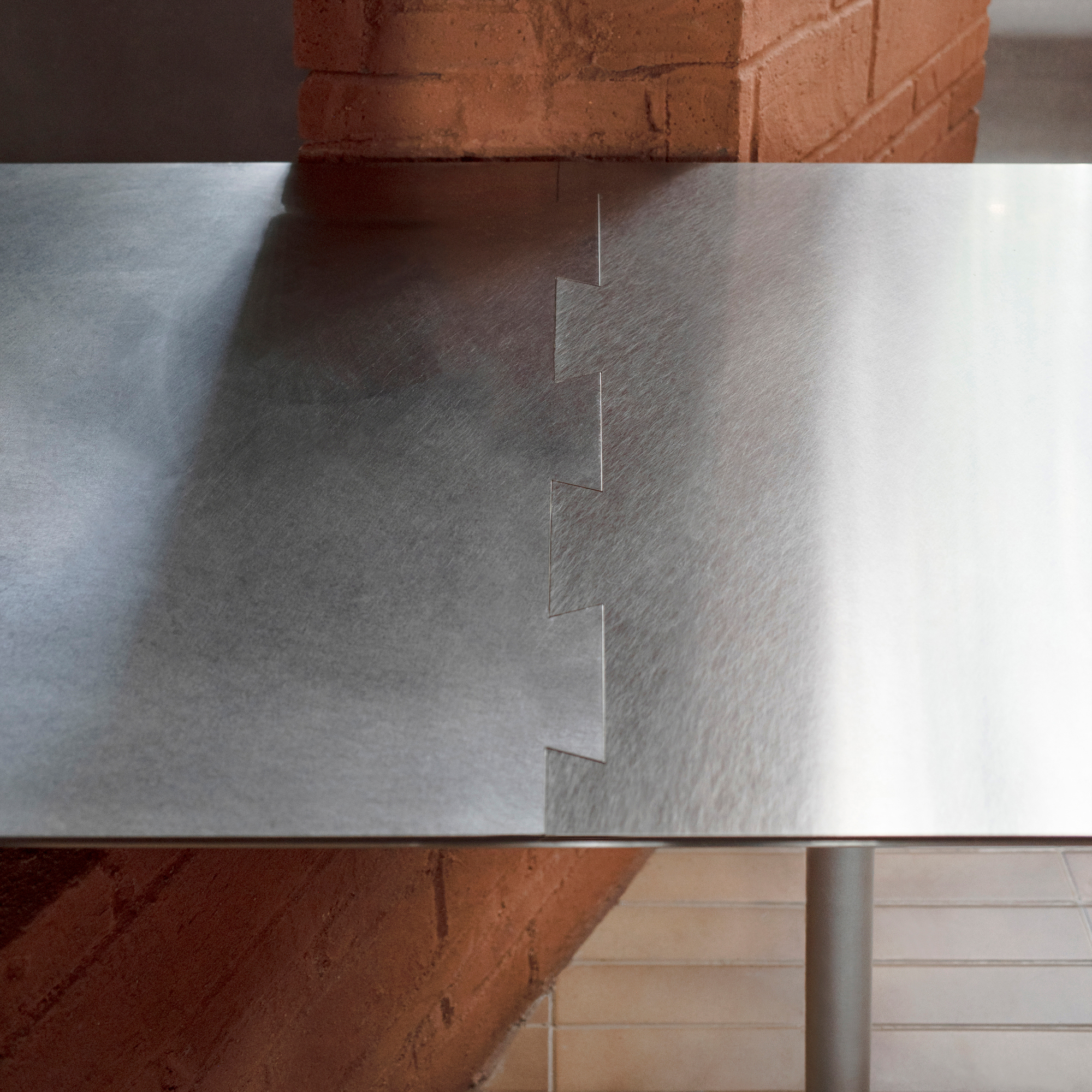 Close-up of the welded joints connecting brushed steel table legs against red brick masonry