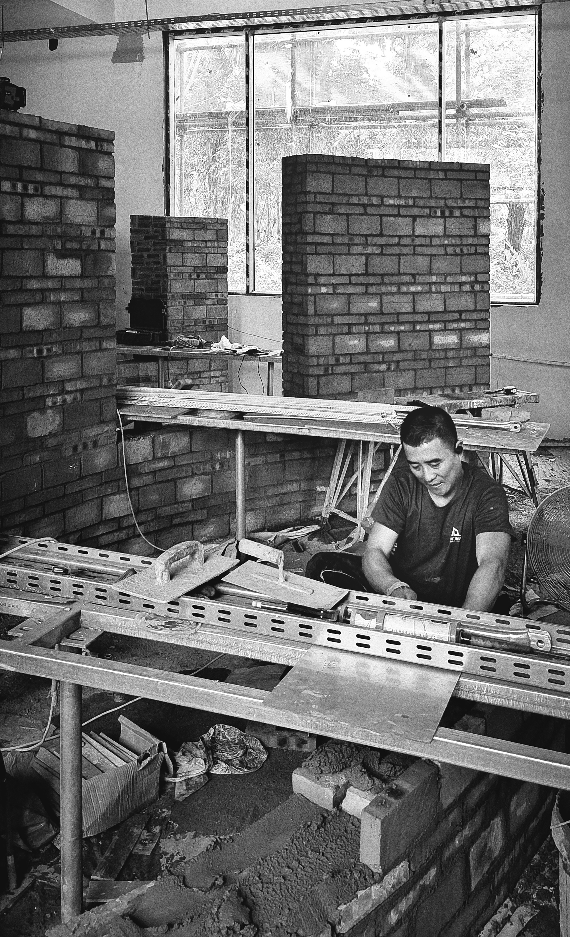 Worker assembling perforated metal tables among brick partition walls during construction