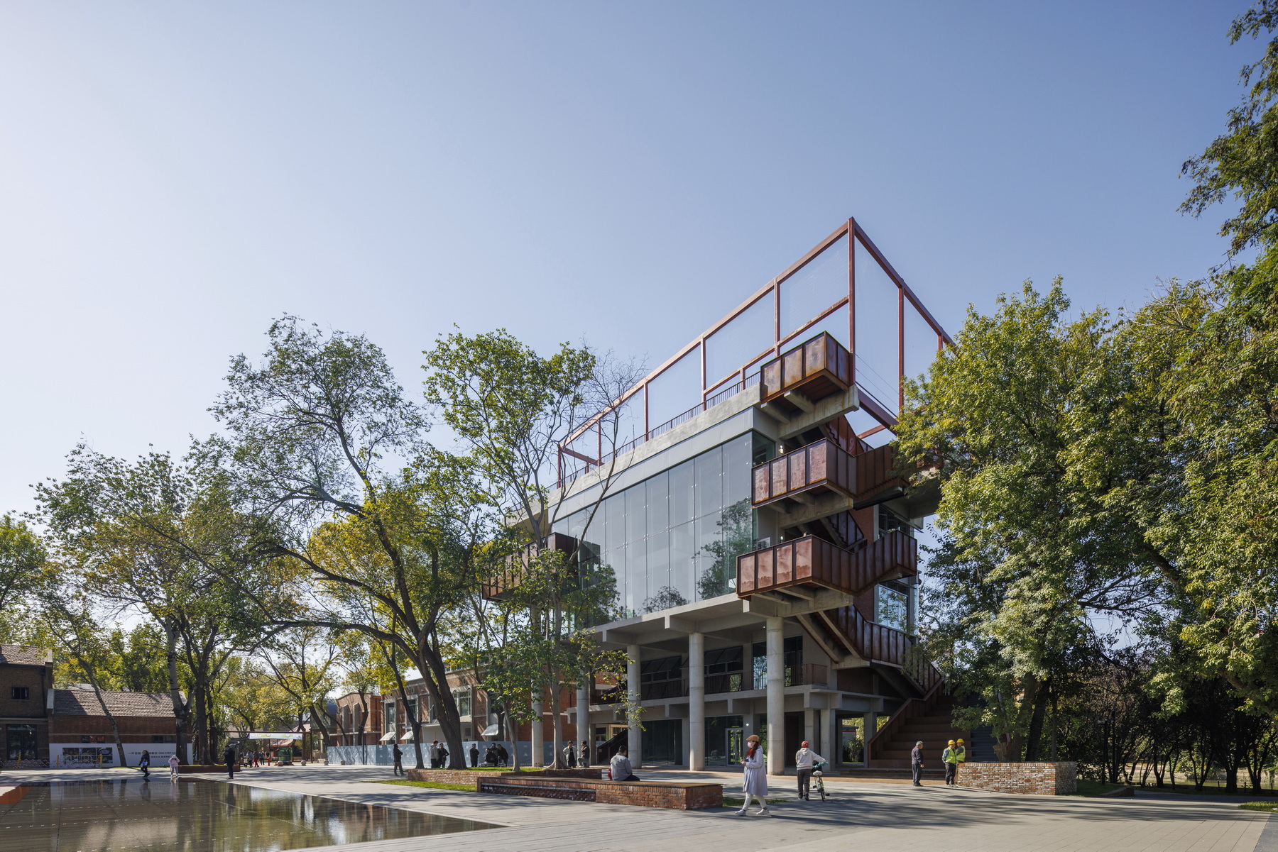 Elevated view of the multi-story structure with red steel frame and reflecting pool in the foreground