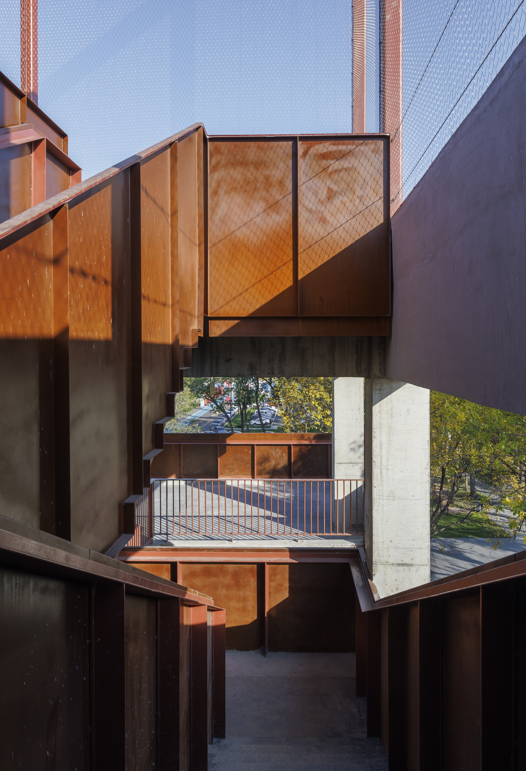 Framed view through stacked weathered steel balconies and concrete floor slabs at dusk