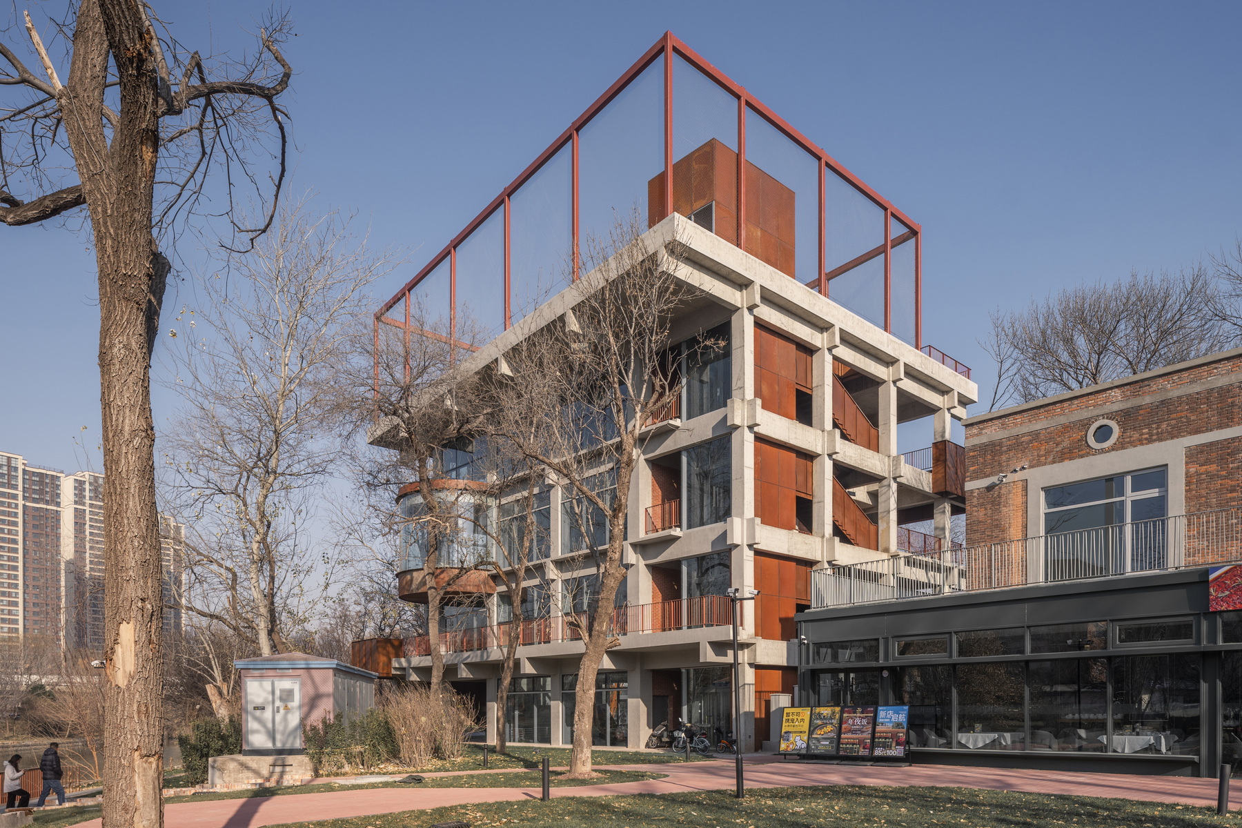 Street facade with exposed concrete columns at ground level and weathered steel cladding on upper floors in winter
