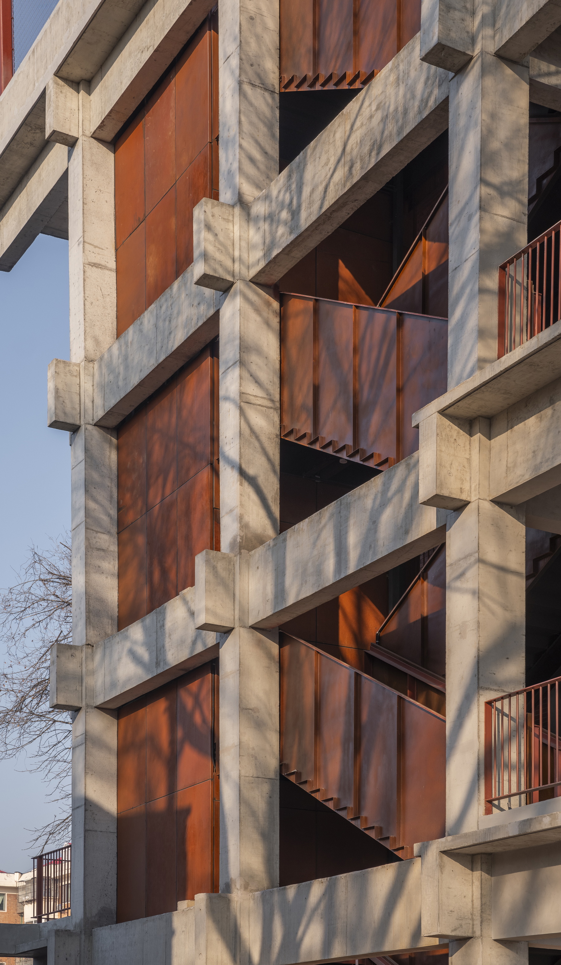 Facade detail showing diagonal tree shadows cast across weathered steel panels and concrete structural grid