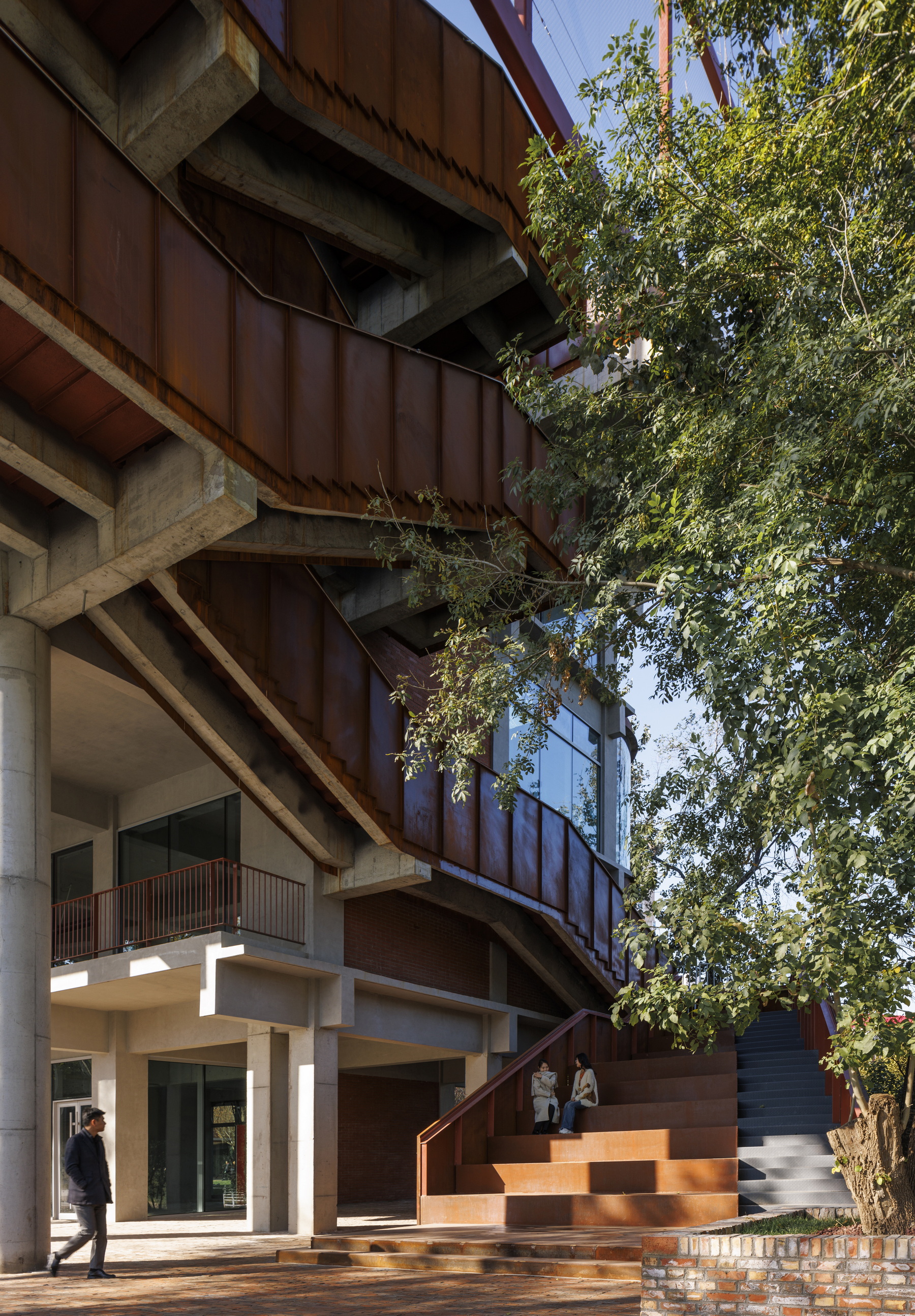 Ground level entrance with stepped weathered steel platform and concrete columns beneath cantilevered upper floors