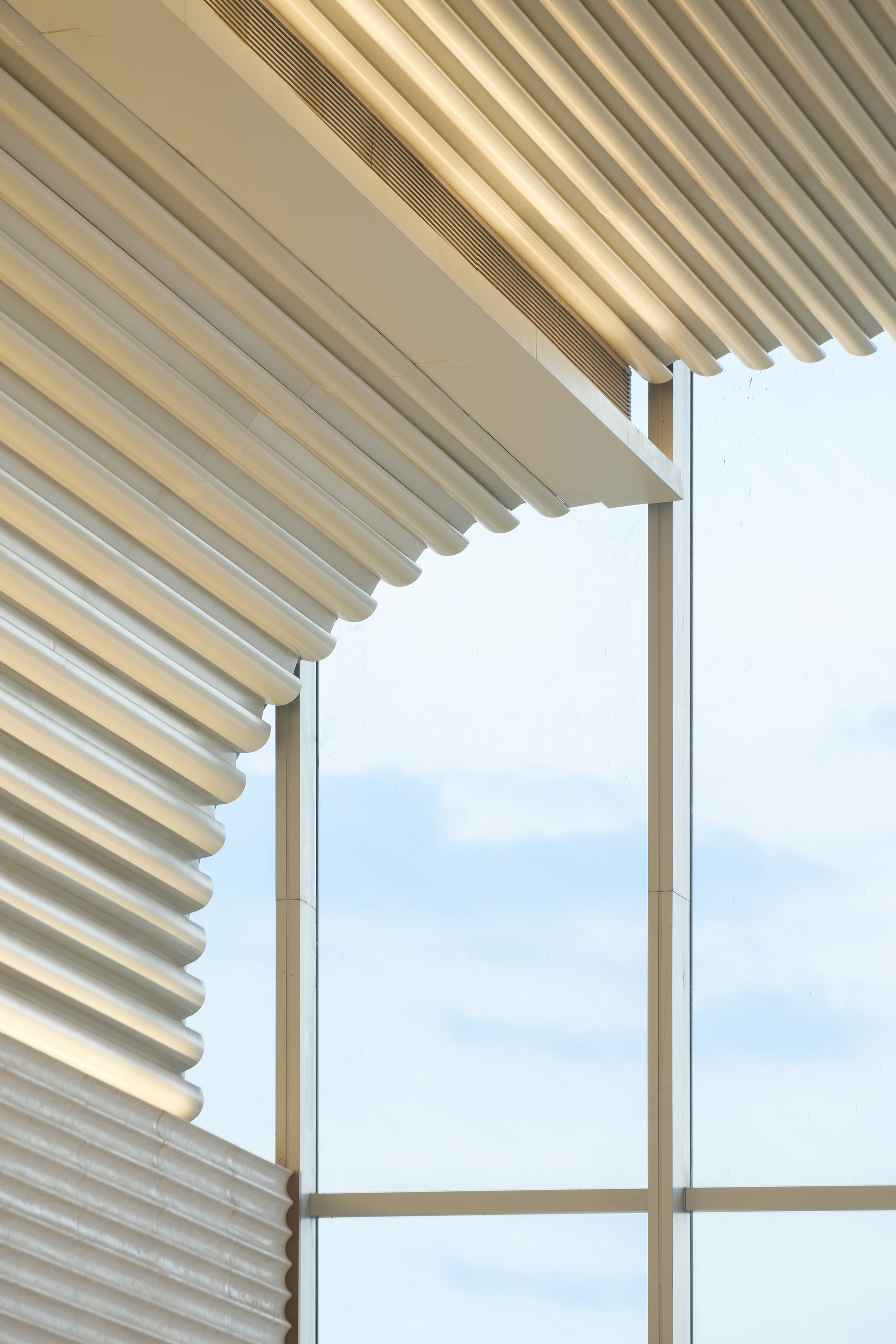 Detail of undulating ceiling ribs meeting the curtain wall corner under pale sky
