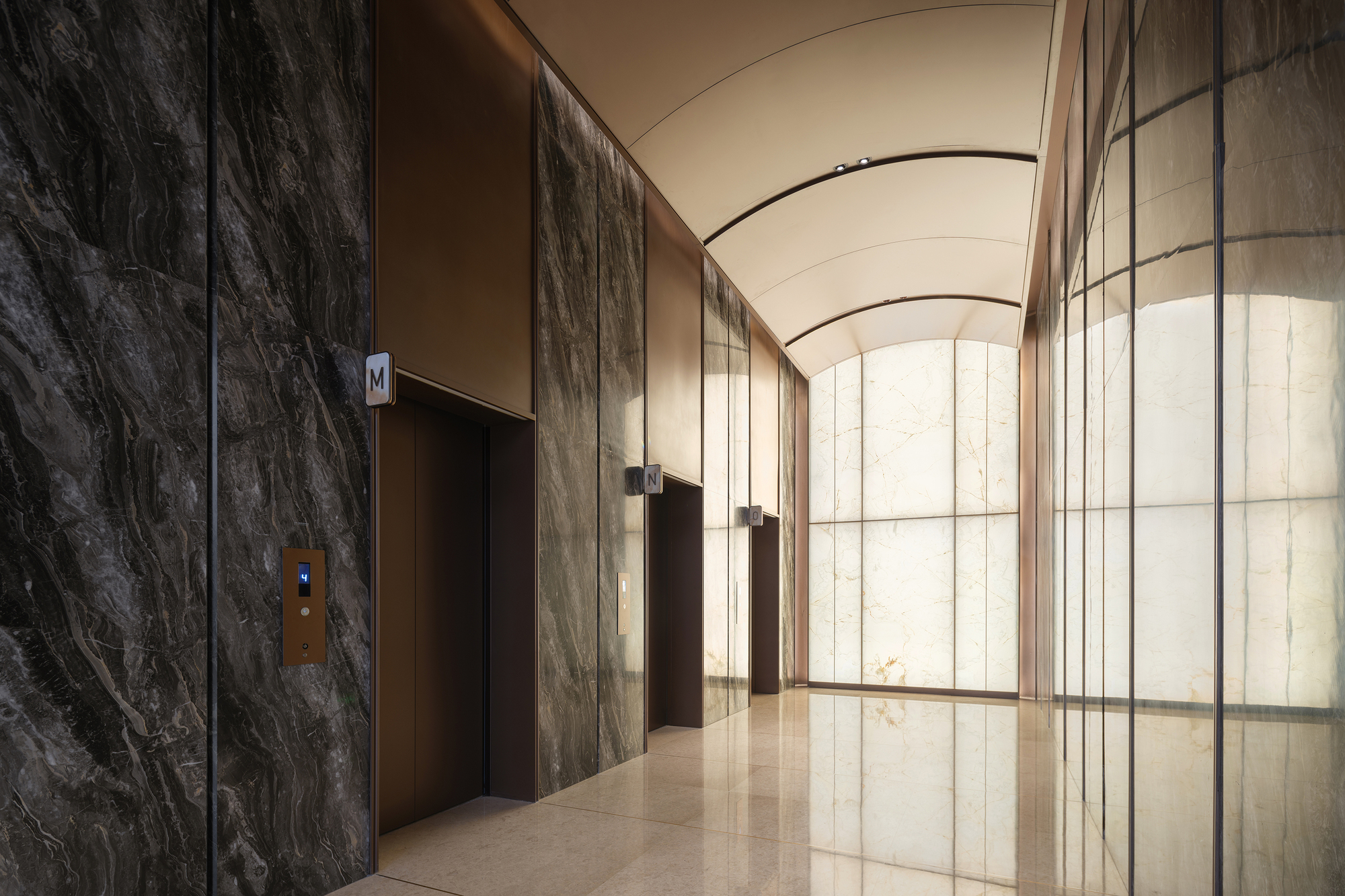 Elevator lobby with dark veined stone walls and arched translucent glass partition under barrel vault ceiling