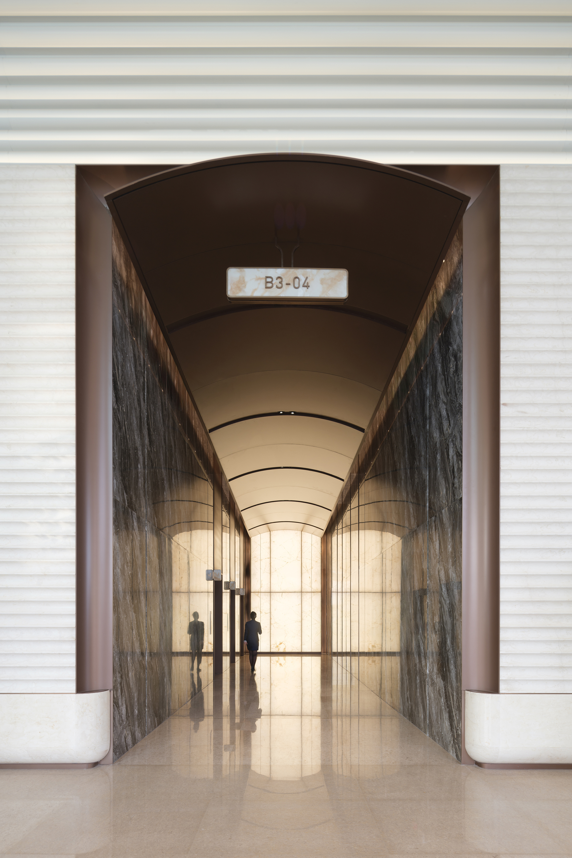 Arched passageway with barrel vault ceiling and veined stone walls framing silhouettes in polished floor reflection