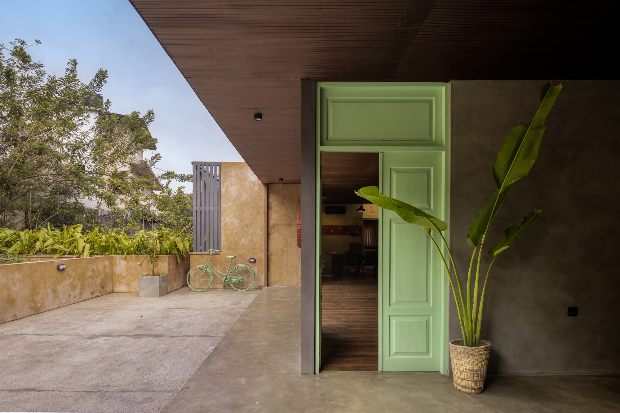 Covered terrace with green paneled door opening to interior and a bicycle leaning against the wall