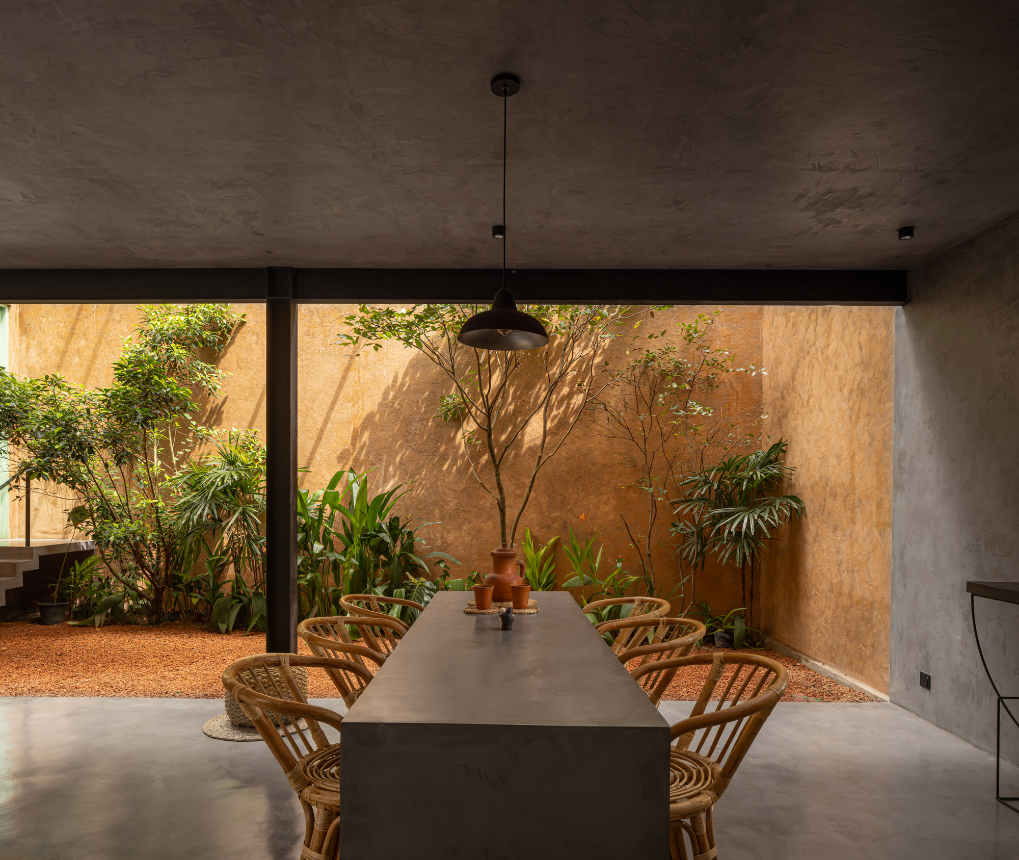 Dining space opening through frameless glass to courtyard with ochre walls and planted beds