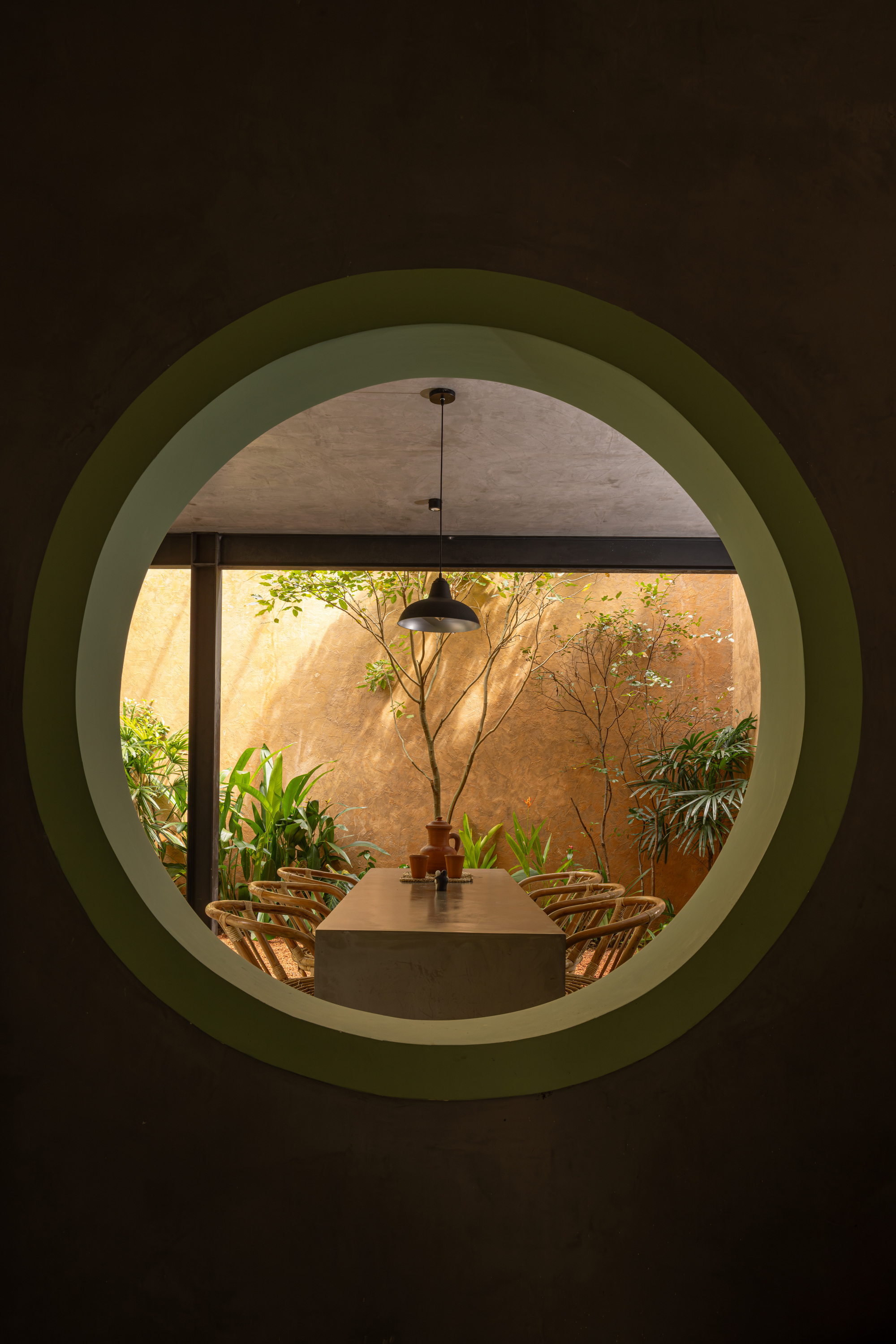 View through circular green portal to dining table and sunlit courtyard with tree