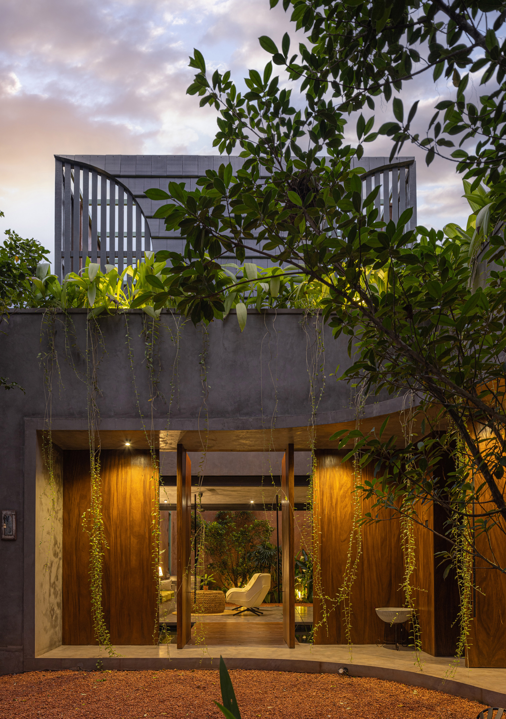 Street facade with timber-clad entry, rooftop planters and cascading vines under evening clouds