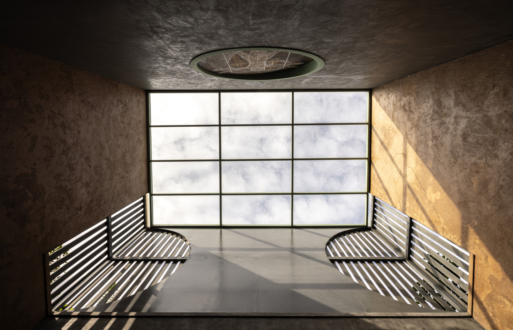 Rooftop terrace with slatted metal benches facing a gridded glass wall and circular skylight
