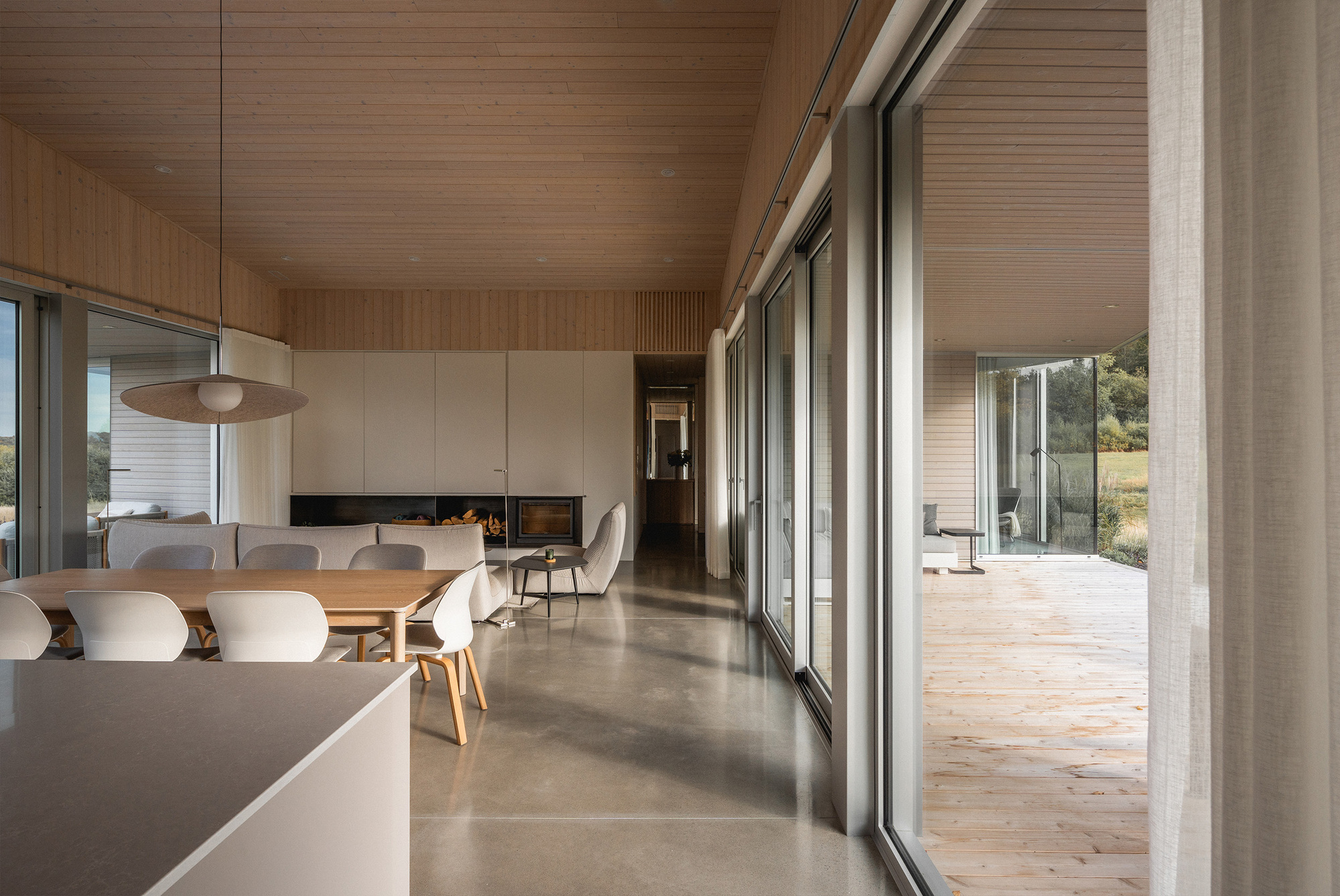 Open living space with polished concrete floor and timber ceiling viewed toward the glazed terrace opening