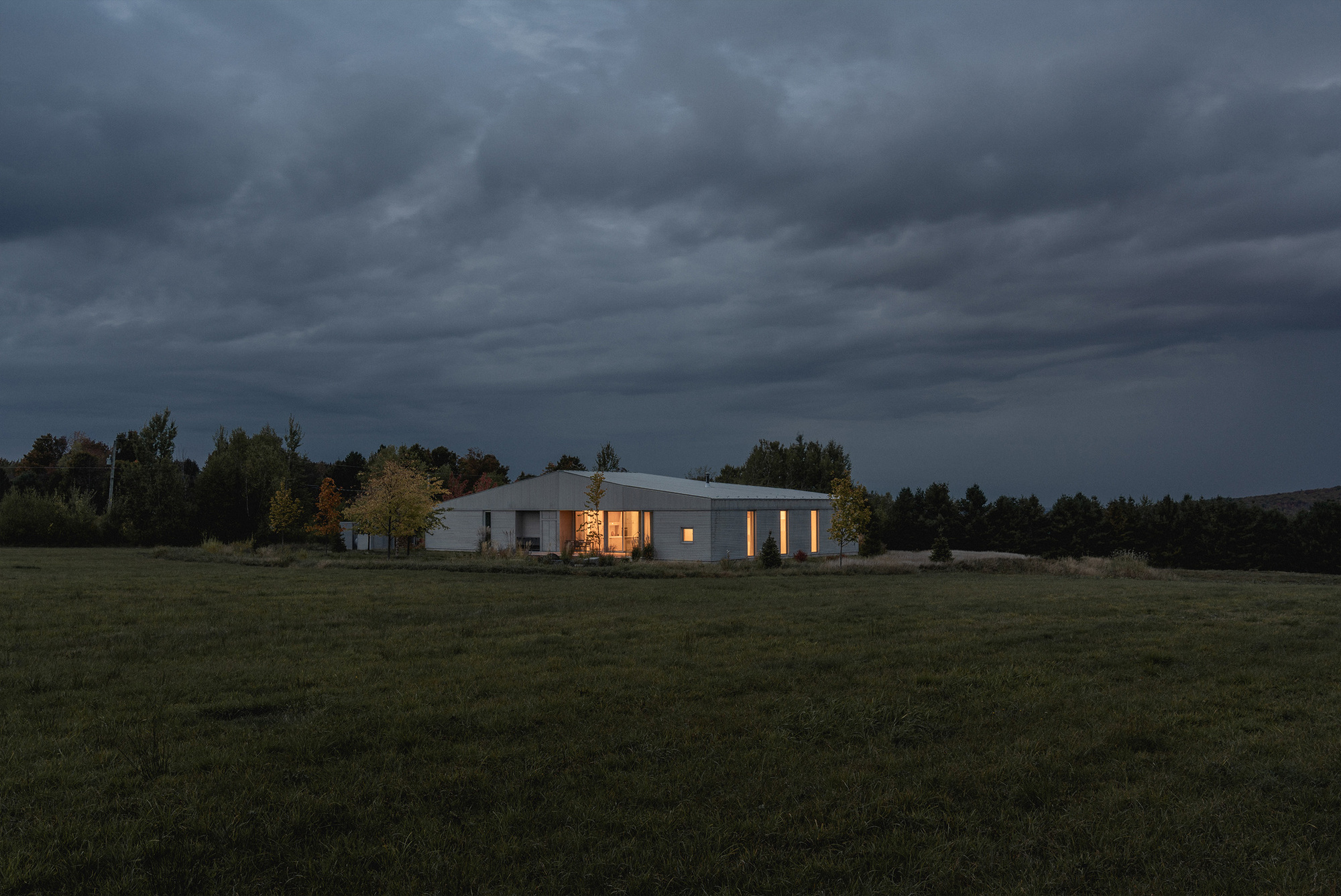 Night view of the illuminated residence across a dark meadow under heavy storm clouds