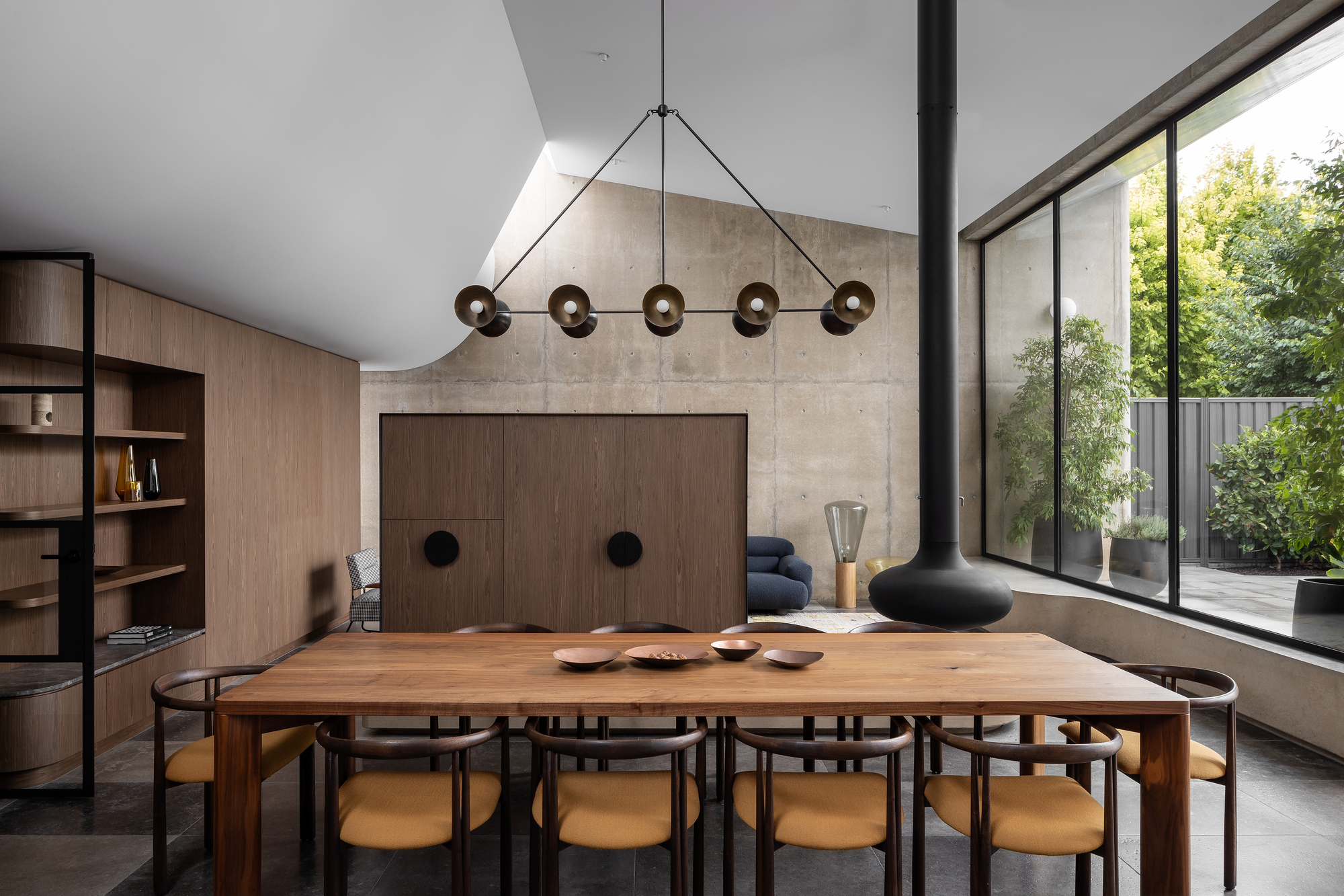 Dining room with timber table beneath a linear pendant light fixture and concrete fireplace surround