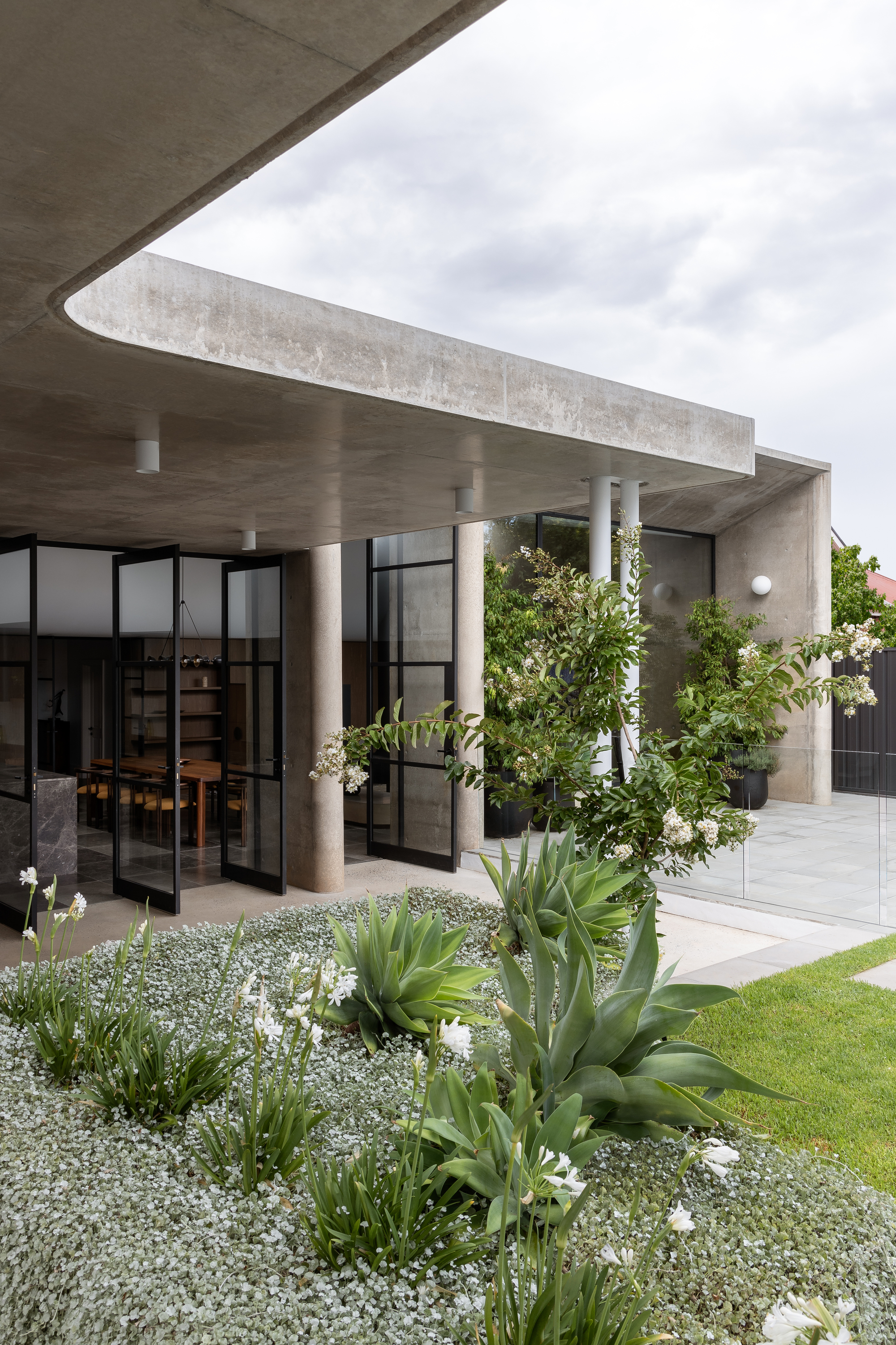 Concrete roof overhang supported by cylindrical columns above planted bed with agave and white gravel