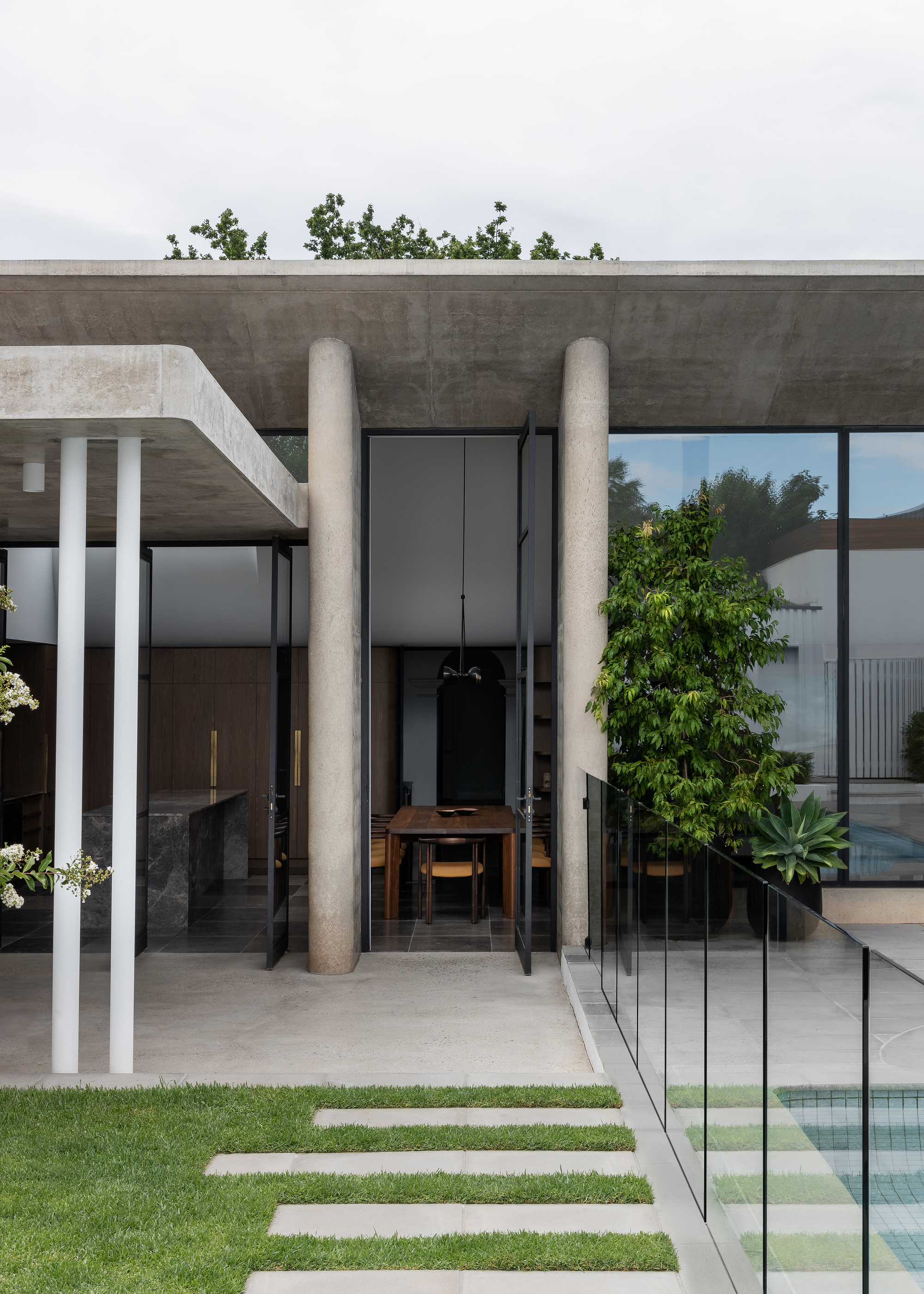 Entrance portico framed by concrete columns with glass balustrade and lawn stepping stones in foreground
