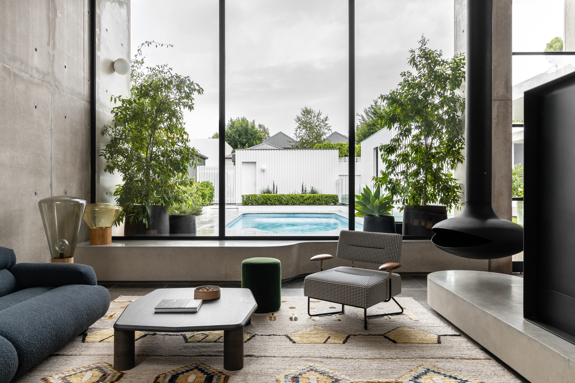 Living room with full-height glazing framing view of outdoor pool and potted trees