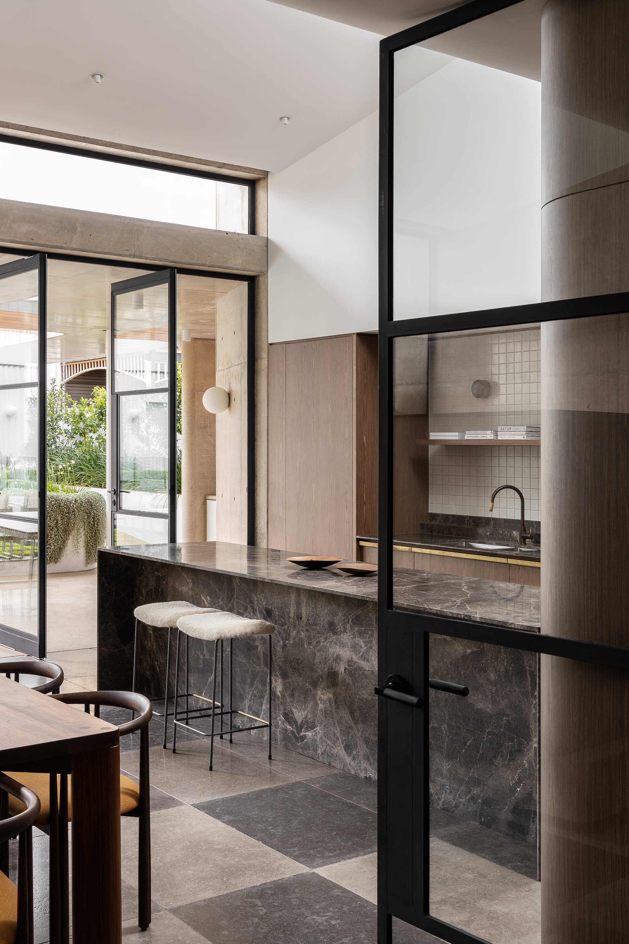 View through steel-framed glass partition to kitchen with stone island and garden beyond