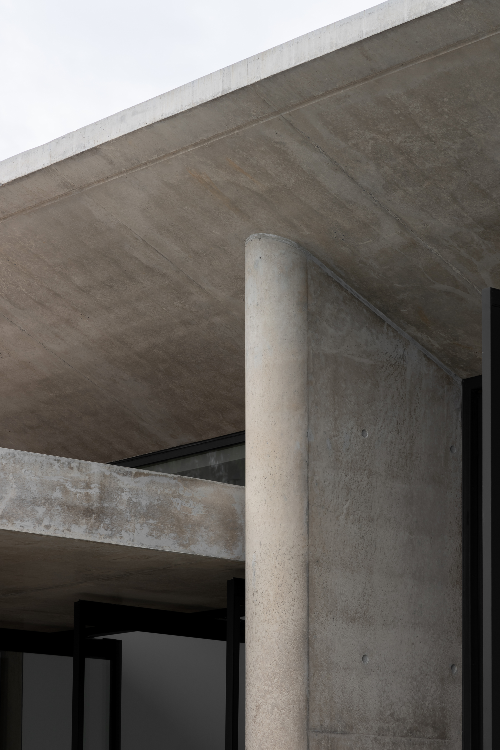 Close-up of cylindrical concrete column meeting soffit and wall planes under overcast sky