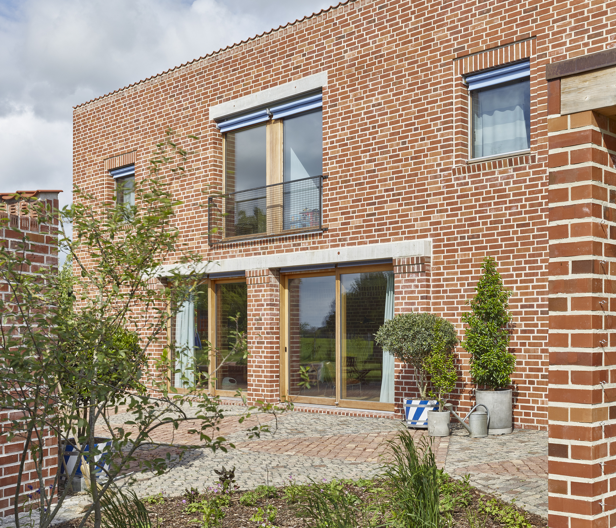 Brick facade detail with paved courtyard terrace and small trees flanking glazed openings