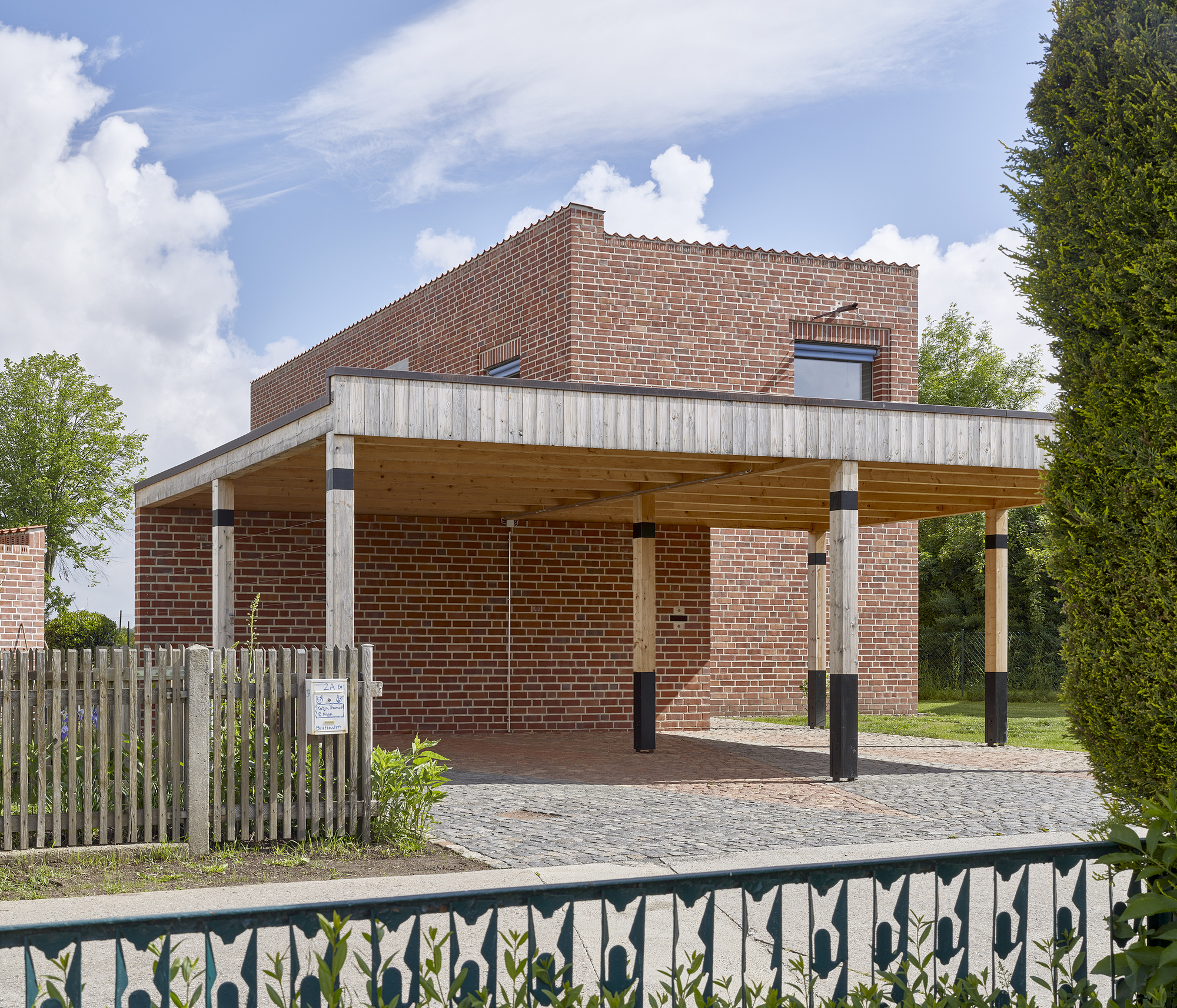 Open carport structure with exposed timber beams and columns against brick wall under cloudy sky