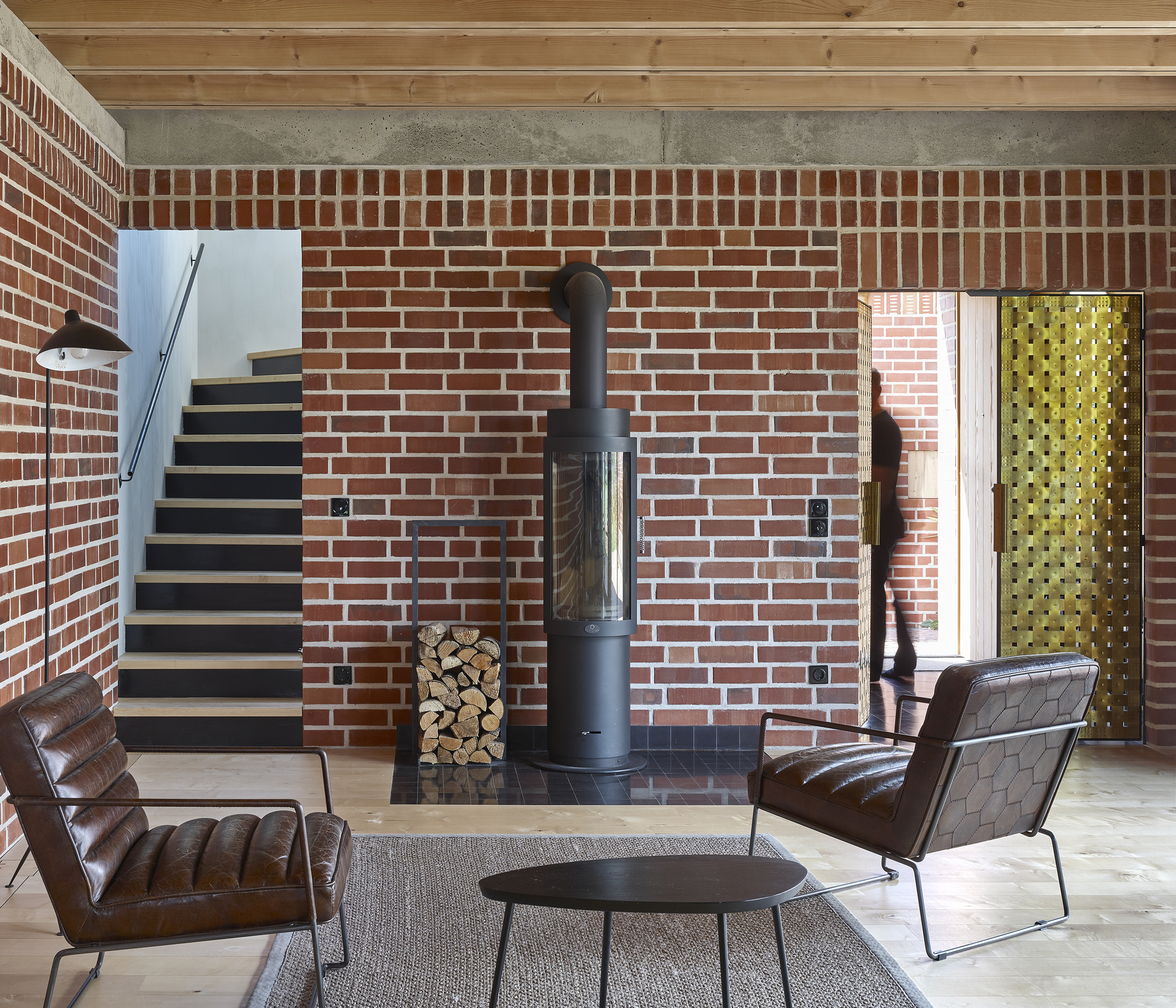 Interior living space with exposed brick wall, freestanding wood stove and floating timber staircase