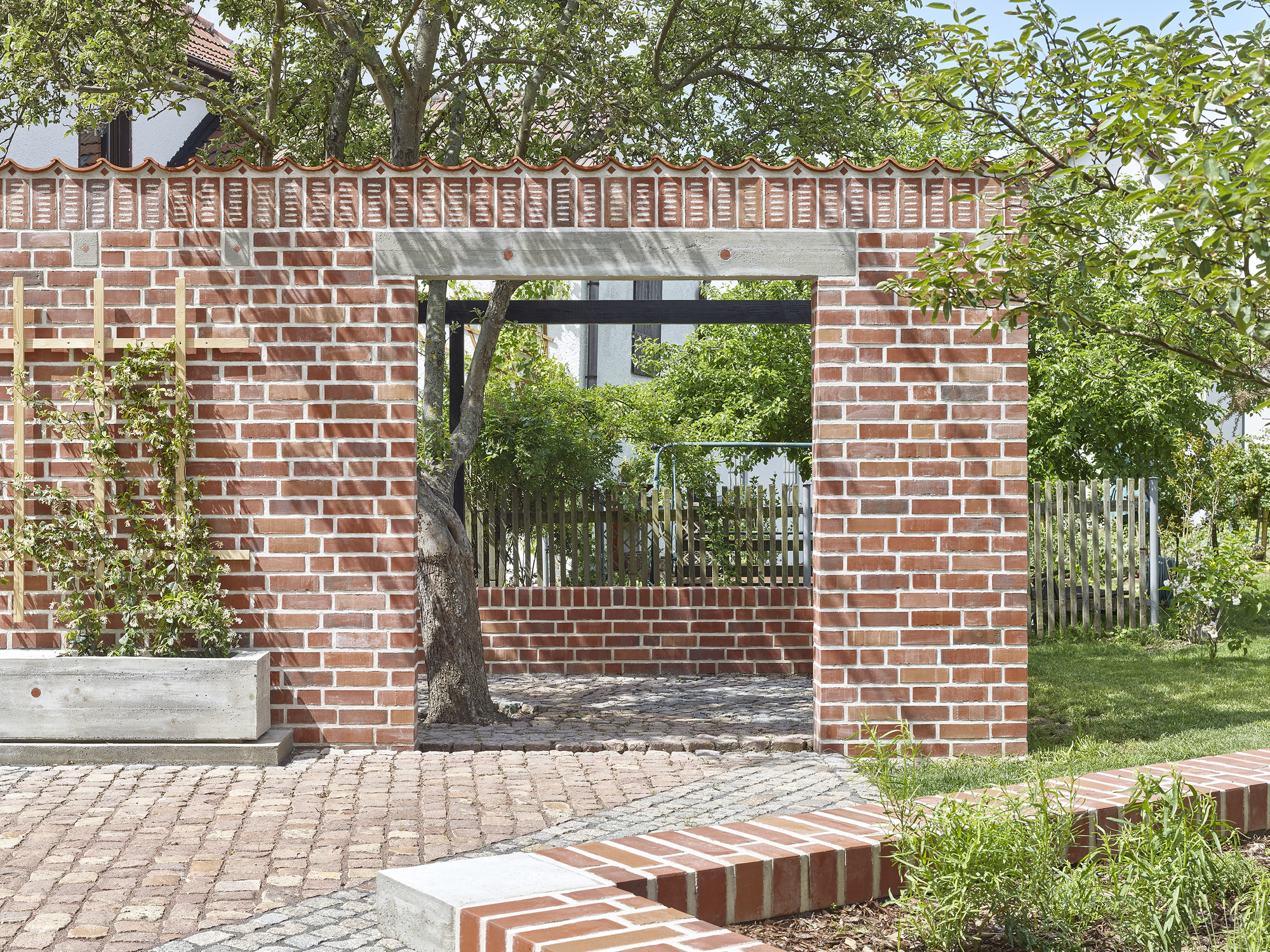 Brick garden portal framing existing tree with concrete lintel and cobblestone paving underfoot
