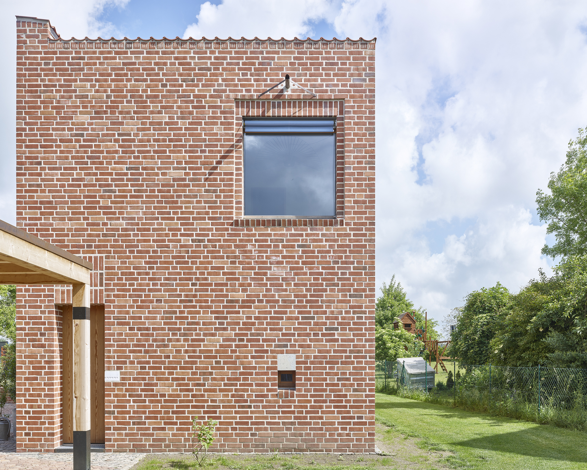 Red brick facade with single recessed window and timber porch entry beneath a cloudy summer sky