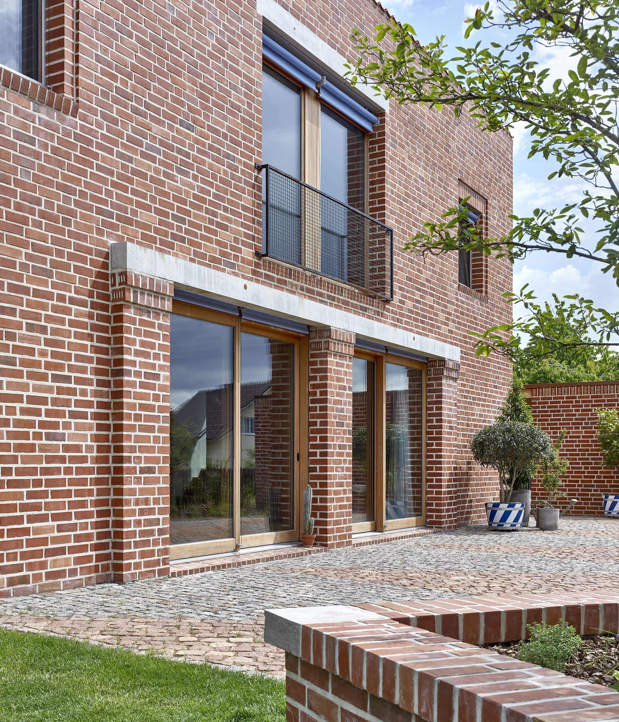 Rear courtyard elevation with sliding glass doors and upper balcony framed by brick walls and topiary