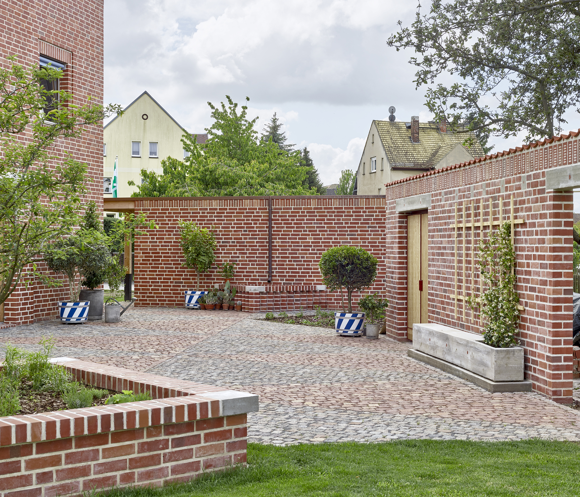 Enclosed brick courtyard with cobblestone paving and concrete planters beneath neighboring gabled roofs